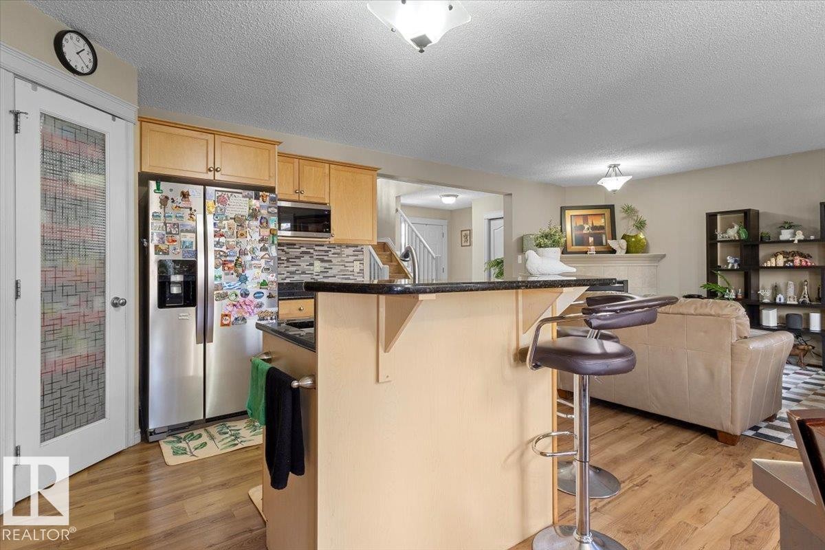 Kitchen featuring wood-finish flooring, light wood cabinetry, stainless steel appliances, and dark countertops - 3356 25 Ave, Edmonton, AB - Indoor