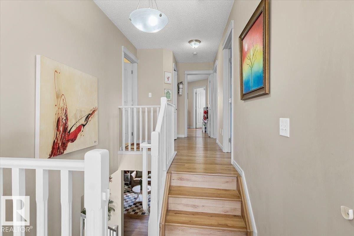 Wood-finish staircase with white balusters leading to an upper-level hallway with complementary wood-finish flooring - 3356 25 Ave, Edmonton, AB - Indoor Photo Showing Other Room