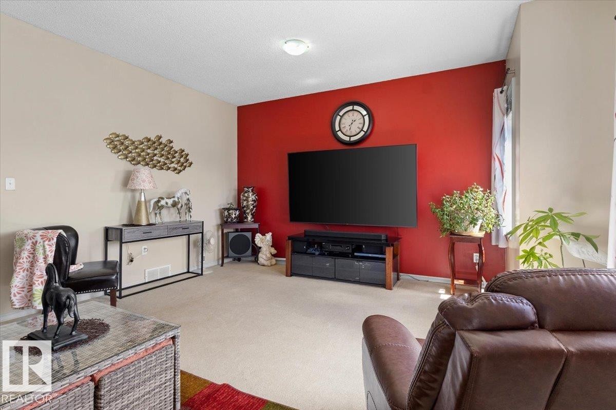 Spacious living area featuring a vibrant accent wall, neutral carpeting, recessed lighting, and ample natural light from a window with vertical blinds - 3356 25 Ave, Edmonton, AB - Indoor Photo Showing Living Room