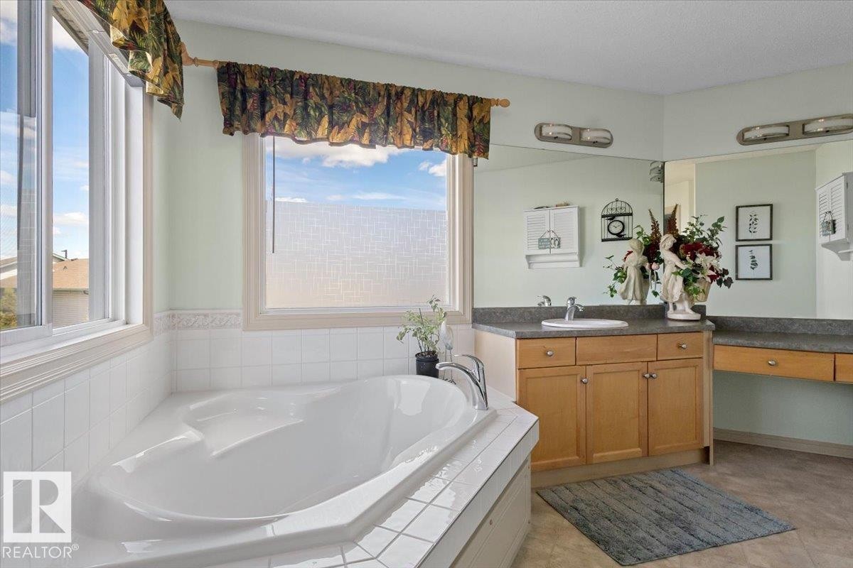 Soaking tub with white tile surround, multiple windows, double vanity with integrated sink, and wood cabinetry - 3356 25 Ave, Edmonton, AB - Indoor Photo Showing Bathroom