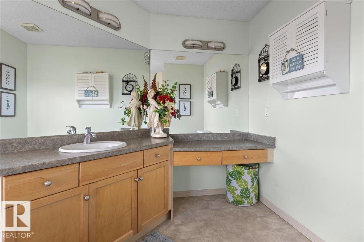 Bathroom vanity featuring a single basin sink, a large mirror, wood-finish cabinetry, gray countertops, and overhead lighting - 3356 25 Ave, Edmonton, AB - Indoor Photo Showing Bathroom