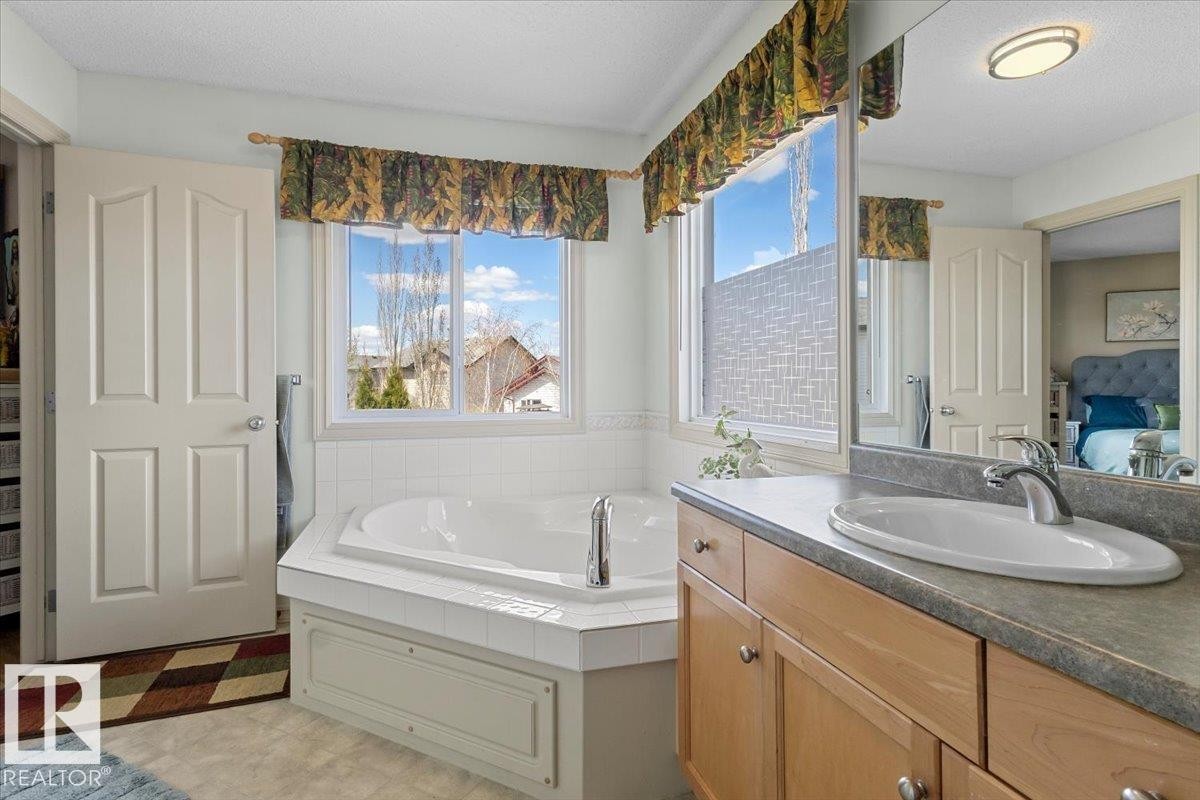 Soaking tub with tiled surround, wood-finish vanity with an integrated sink, and an expansive mirror - 3356 25 Ave, Edmonton, AB - Indoor Photo Showing Bathroom