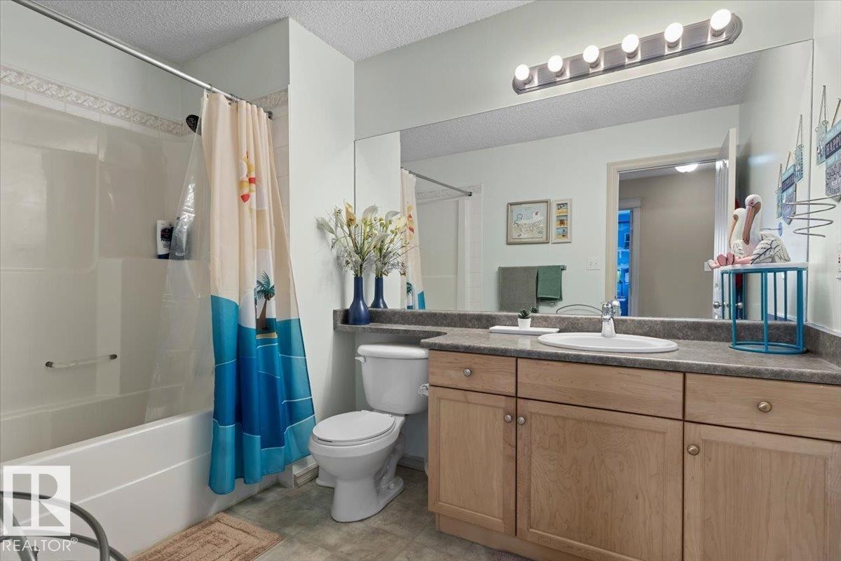 Bathroom featuring a single vanity with wood-finish cabinetry, a large mirror, and a combination shower/tub with a tiled surround - 3356 25 Ave, Edmonton, AB - Indoor Photo Showing Bathroom