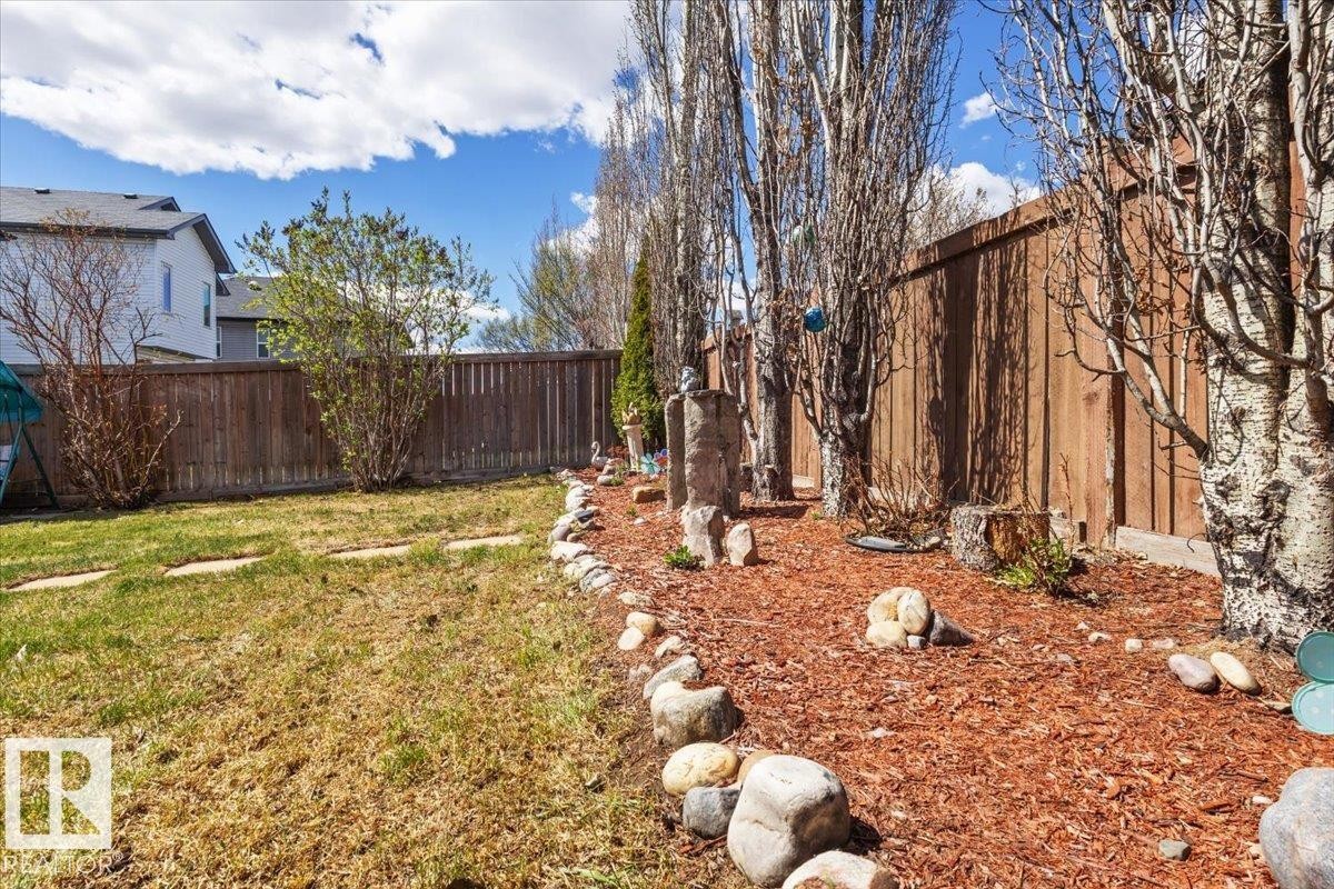 Expansive backyard featuring a manicured lawn, established landscaping with mature trees, and a rock-lined garden bed with wood chip ground cover - 3356 25 Ave, Edmonton, AB - Outdoor
