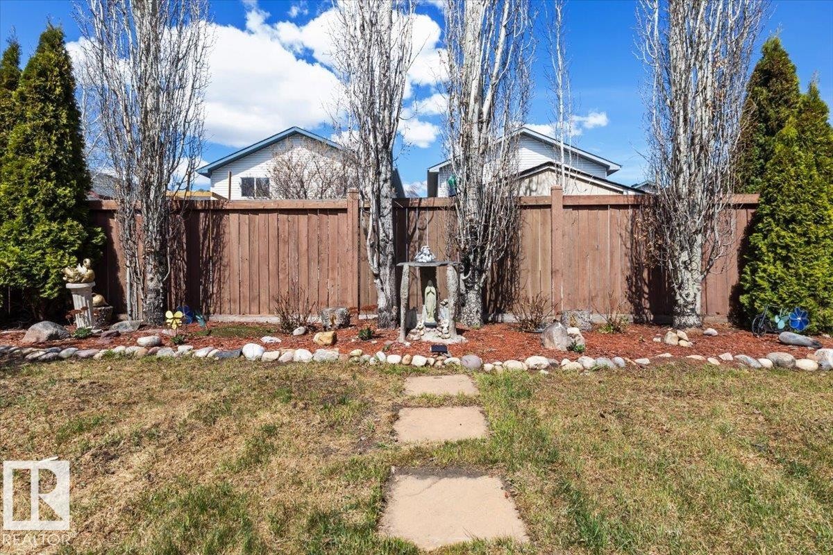 Expansive backyard featuring a stepping stone pathway, a timber privacy fence, and mature evergreen trees - 3356 25 Ave, Edmonton, AB - Outdoor