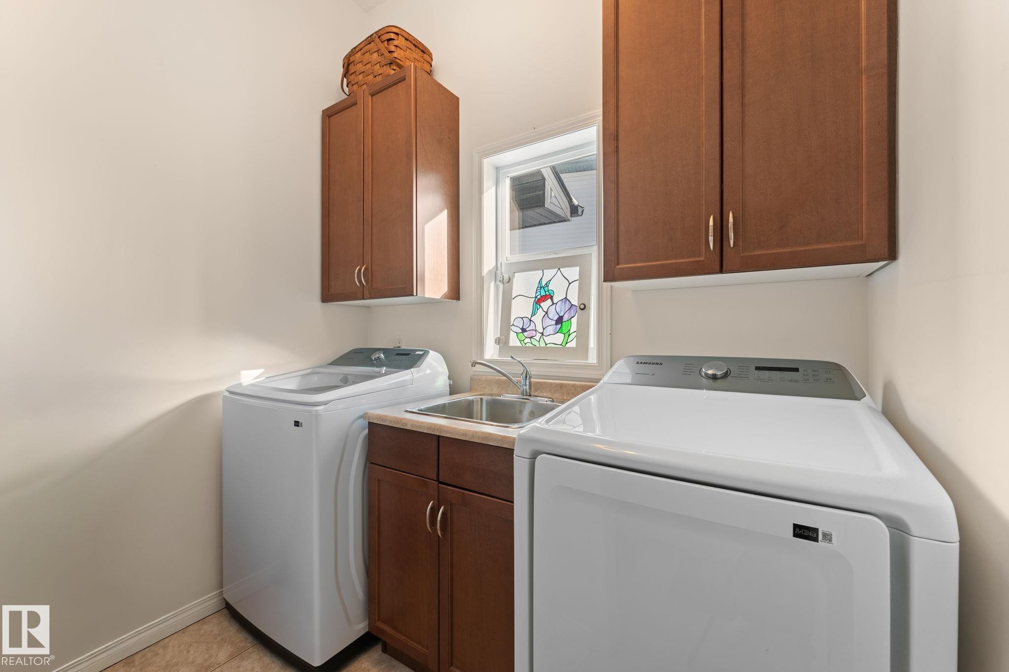 Laundry area featuring built-in cabinetry, utility sink, and a stained-glass window accent - 112 Lakeland Point(E), Beaumont, AB - Indoor Photo Showing Laundry Room