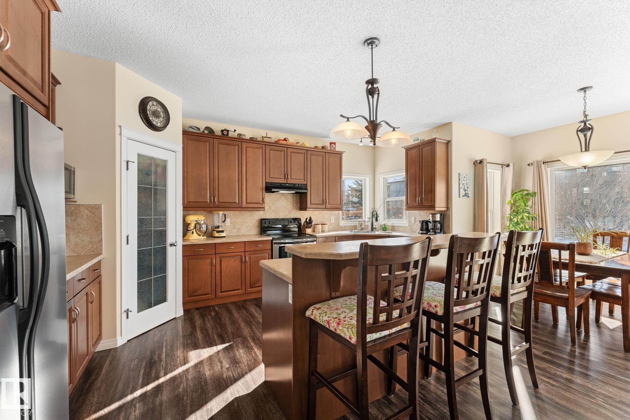 Kitchen featuring wood-finish flooring, warm-toned cabinetry, stainless steel refrigerator, and a kitchen island with bar seating - 112 Lakeland Point(E), Beaumont, AB - Indoor