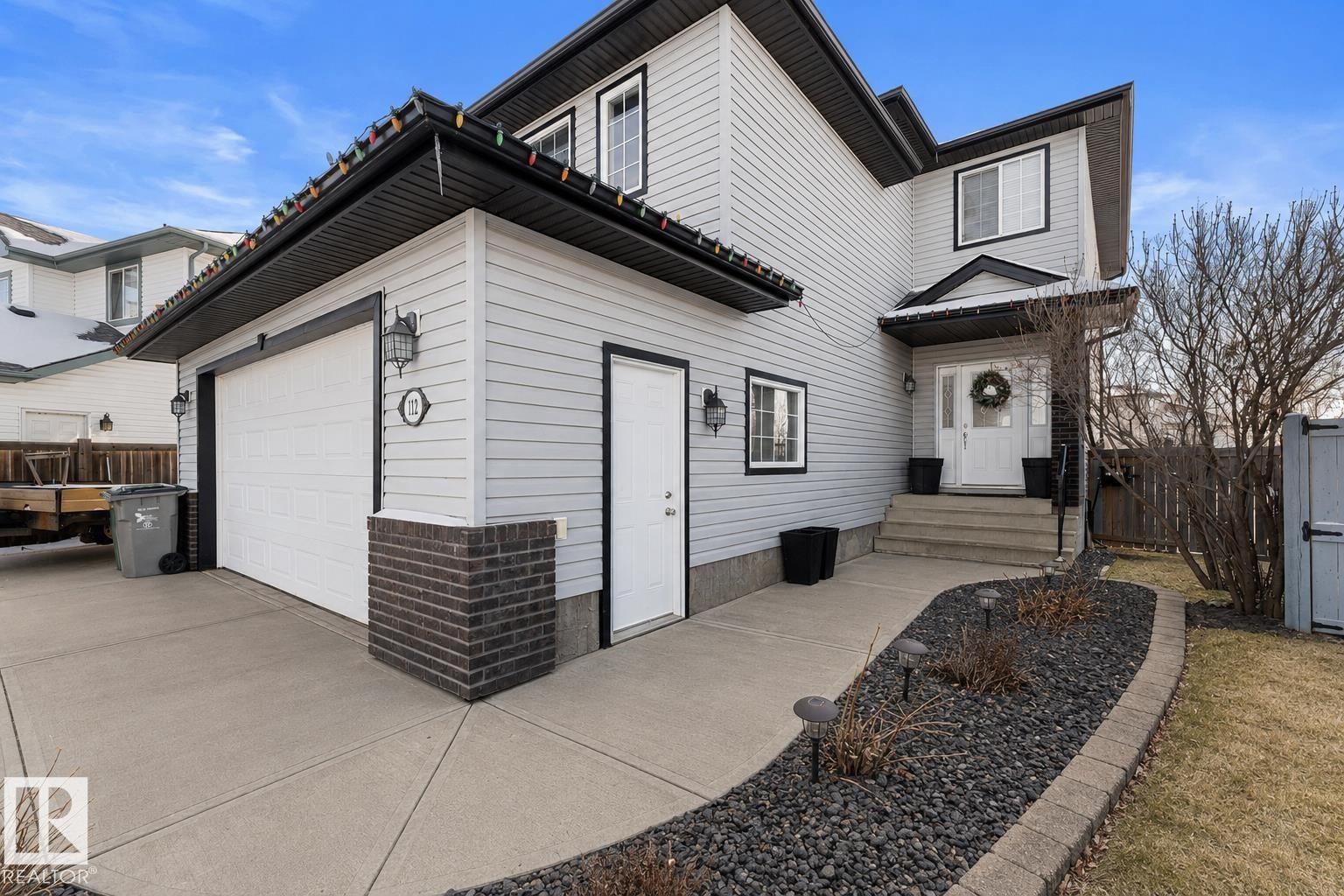 Two-story residence featuring light gray siding with dark trim, a two-car garage, and a concrete driveway - 112 Lakeland Point(E), Beaumont, AB - Outdoor
