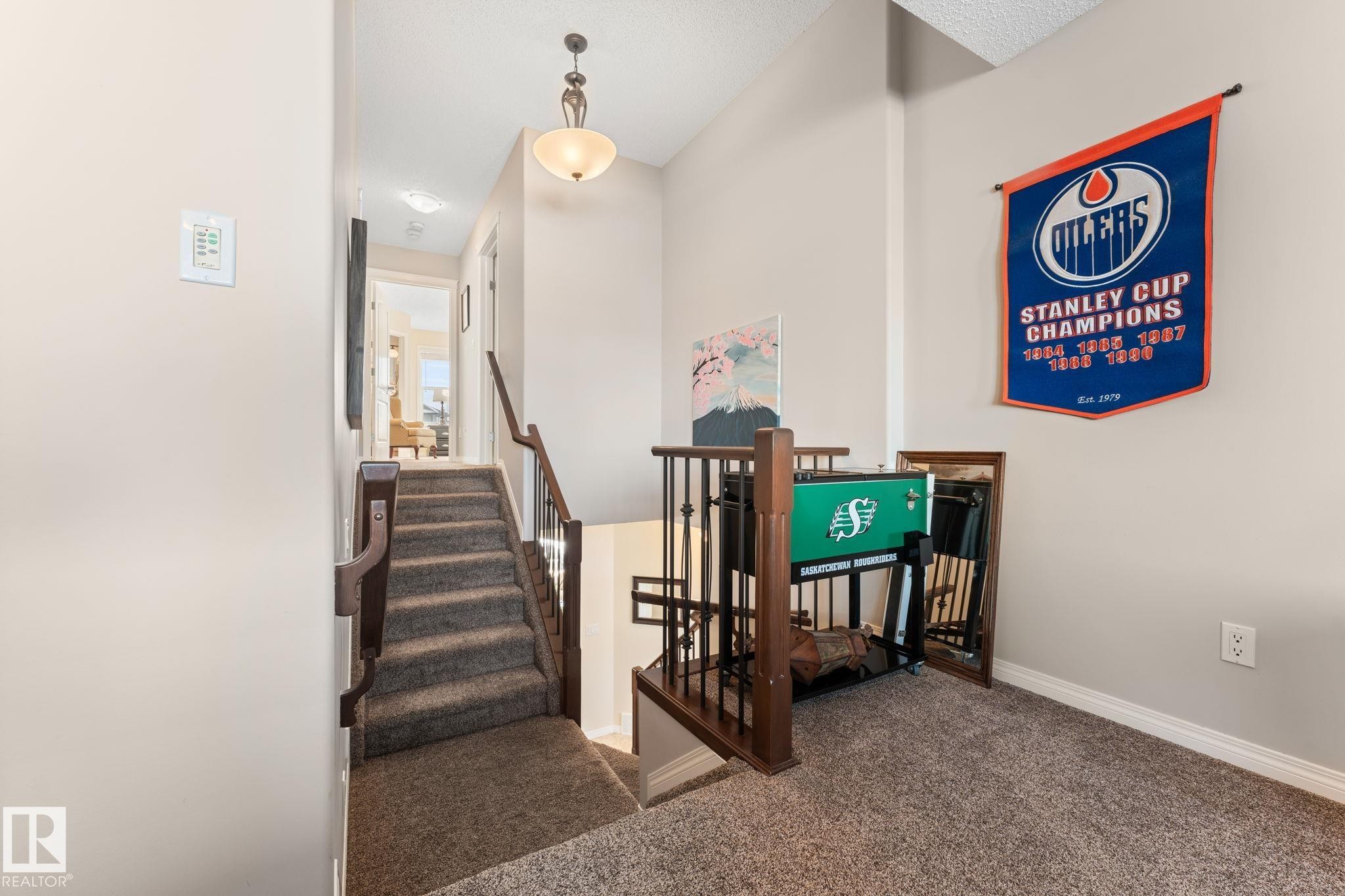 Carpeted staircase featuring a dark wood handrail and balusters, leading to an upper-level hallway with a decorative pendant light fixture - 112 Lakeland Point(E), Beaumont, AB - Indoor Photo Showing Other Room