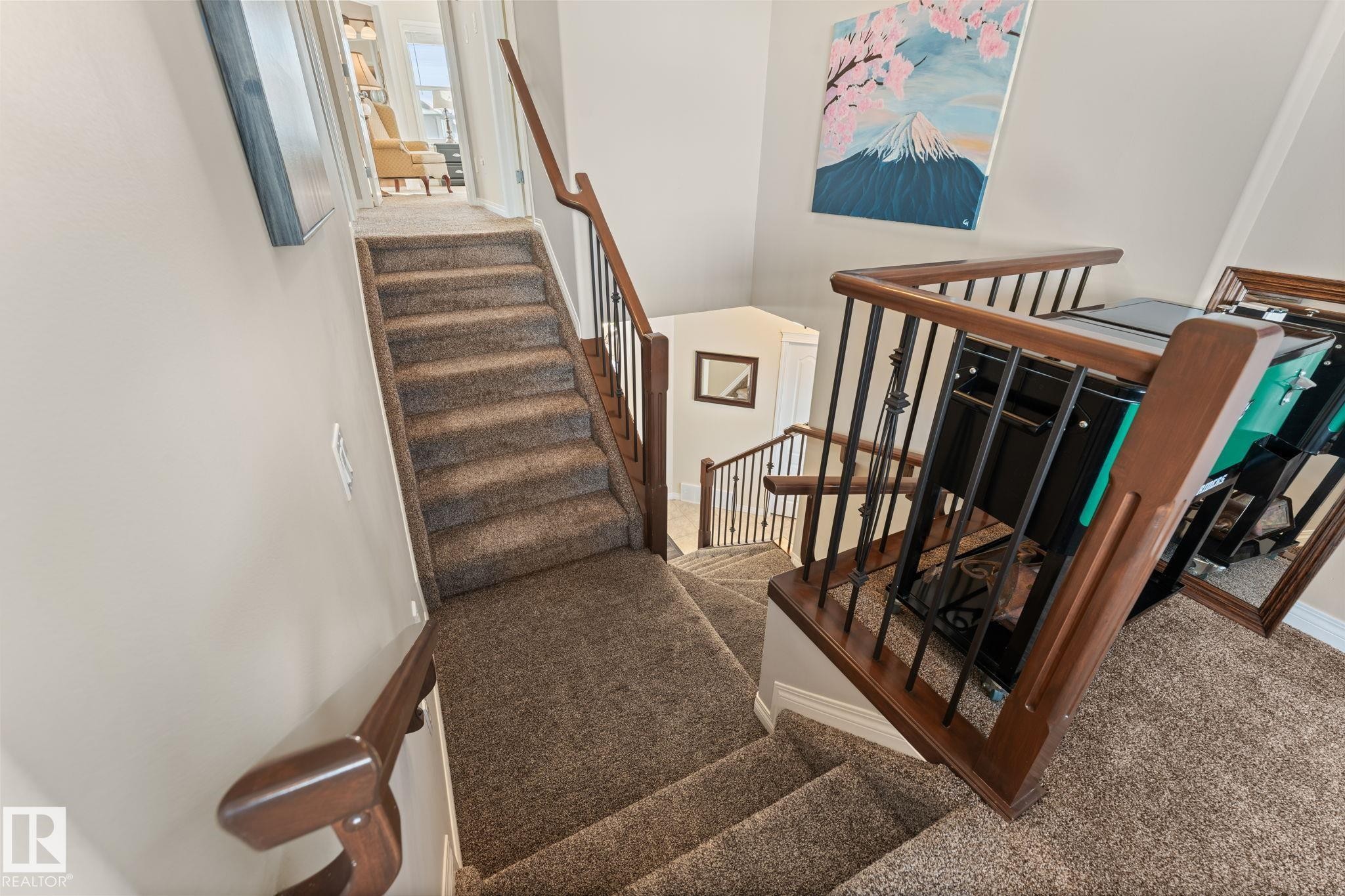 Multi-level staircase featuring neutral-toned carpeted treads, wood handrails, and black metal balusters - 112 Lakeland Point(E), Beaumont, AB - Indoor Photo Showing Other Room