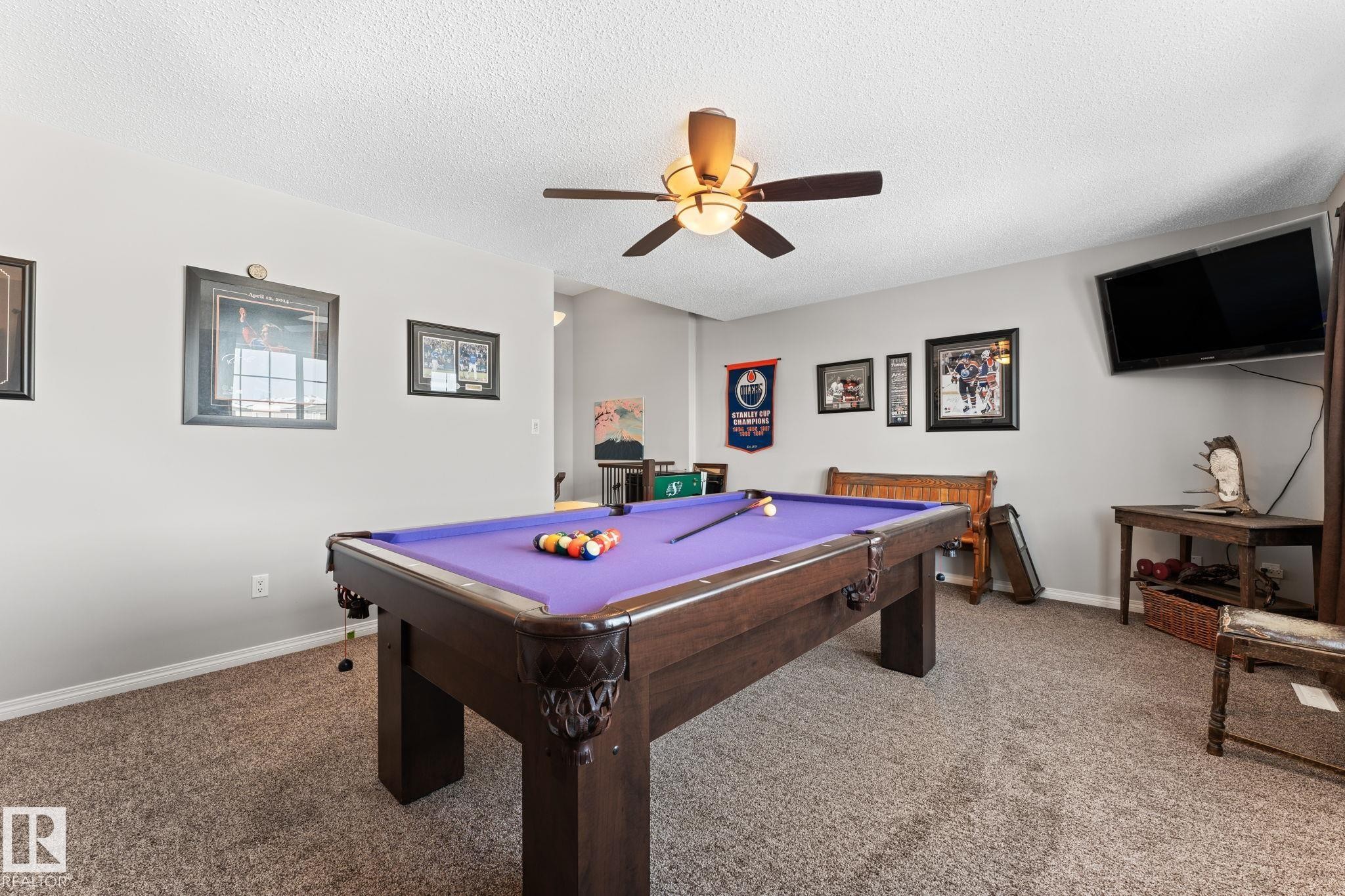 Recreation room featuring a pool table with a purple felt surface, textured carpeting, a ceiling fan with integrated lighting, and neutral wall paint - 112 Lakeland Point(E), Beaumont, AB - Indoor Photo Showing Other Room