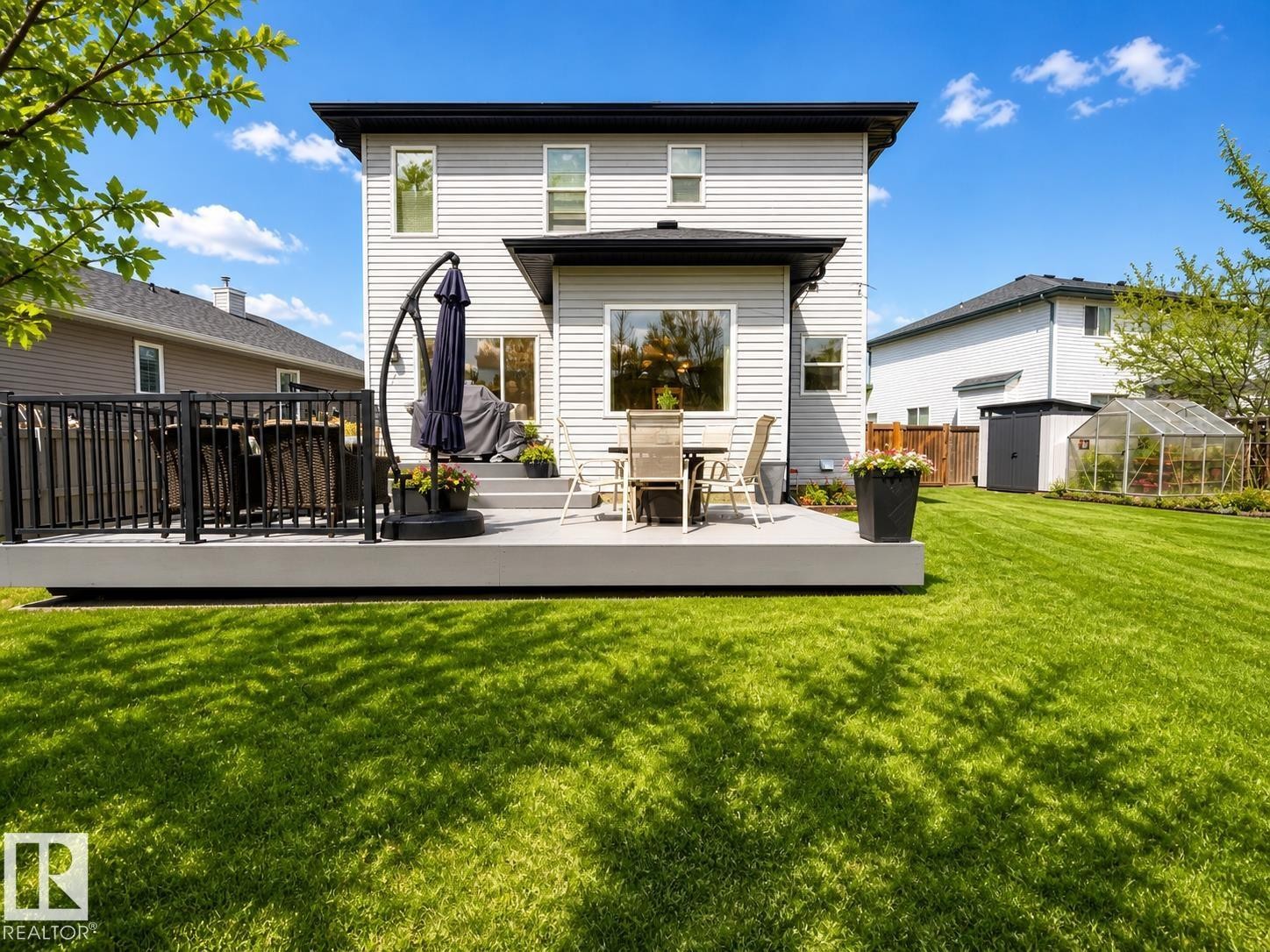 Spacious rear yard featuring a large composite deck with black railings, a dedicated dining area, a storage shed, and a greenhouse - 112 Lakeland Point(E), Beaumont, AB - Outdoor With Deck Patio Veranda