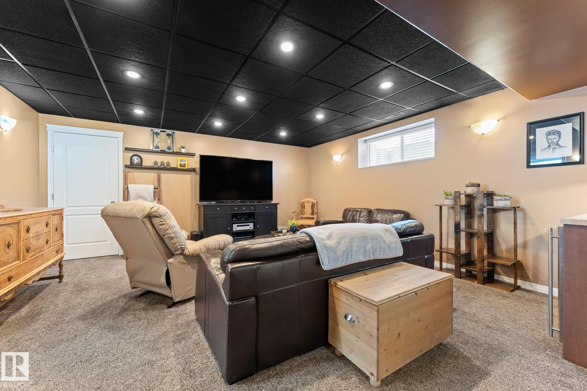 Spacious living area featuring a black grid ceiling with recessed lighting, neutral-toned walls, and grey carpeting - 112 Lakeland Point(E), Beaumont, AB - Indoor Photo Showing Basement