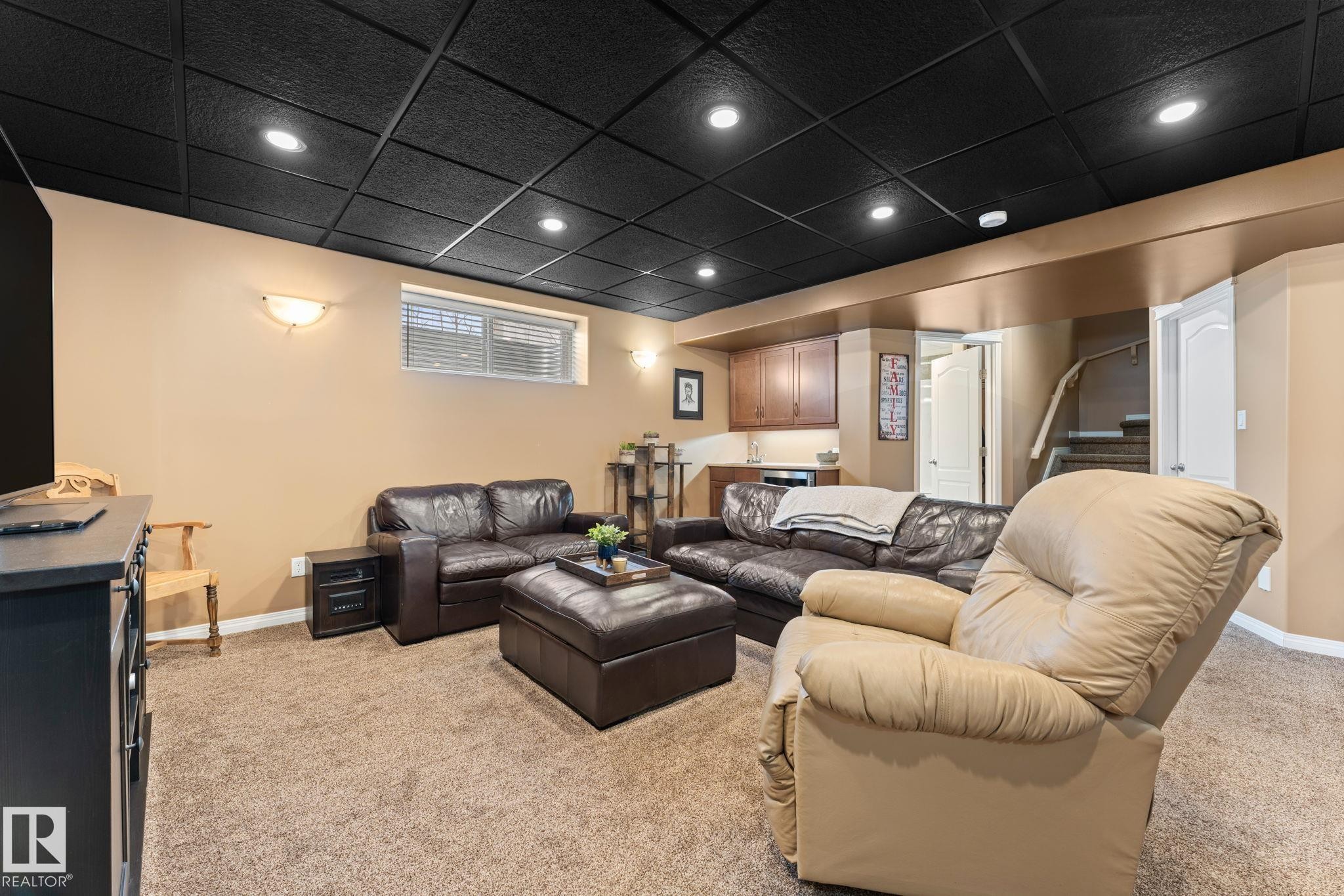 Lower-level living space featuring a black grid ceiling with recessed lighting, beige walls, and carpet flooring - 112 Lakeland Point(E), Beaumont, AB - Indoor Photo Showing Basement