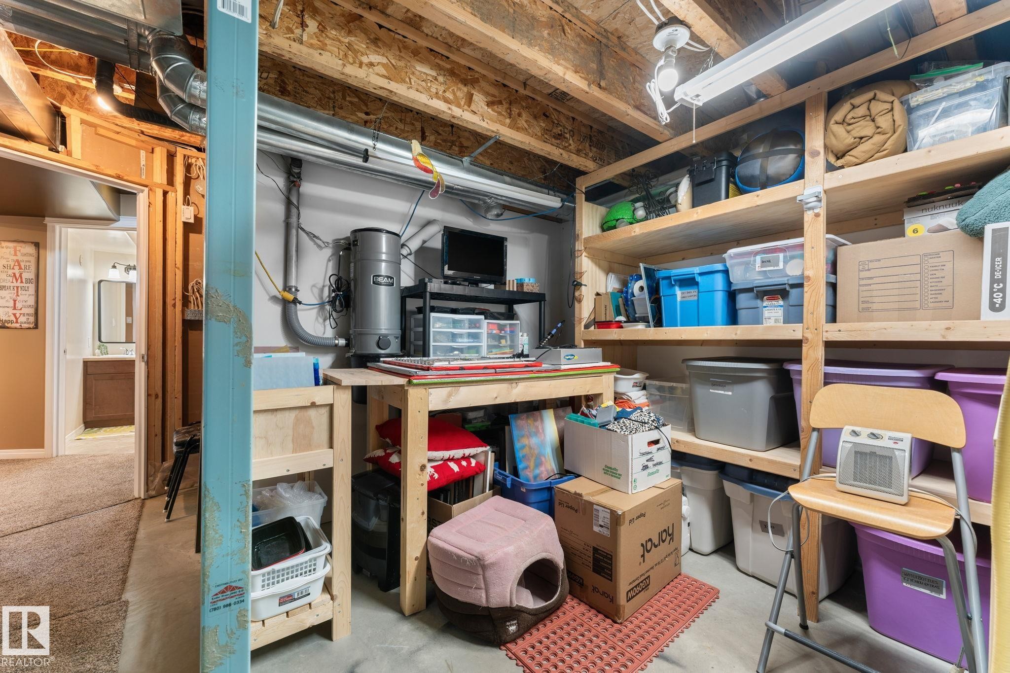 Unfinished basement area featuring exposed wooden joists, concrete flooring, built-in wooden shelving, a workbench, and a central vacuum system - 112 Lakeland Point(E), Beaumont, AB - Indoor