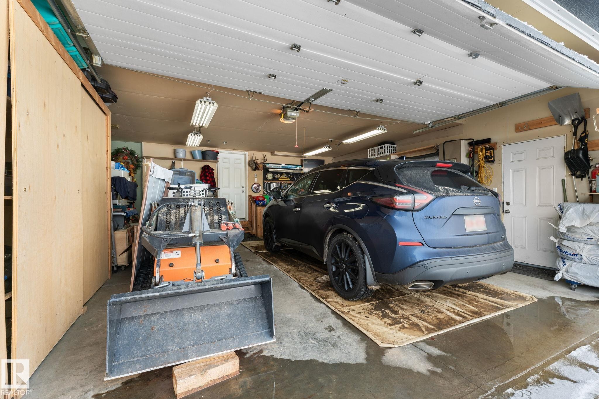 Attached multi-car garage featuring a white paneled overhead door, concrete flooring, and fluorescent ceiling lighting - 112 Lakeland Point(E), Beaumont, AB - Indoor Photo Showing Garage