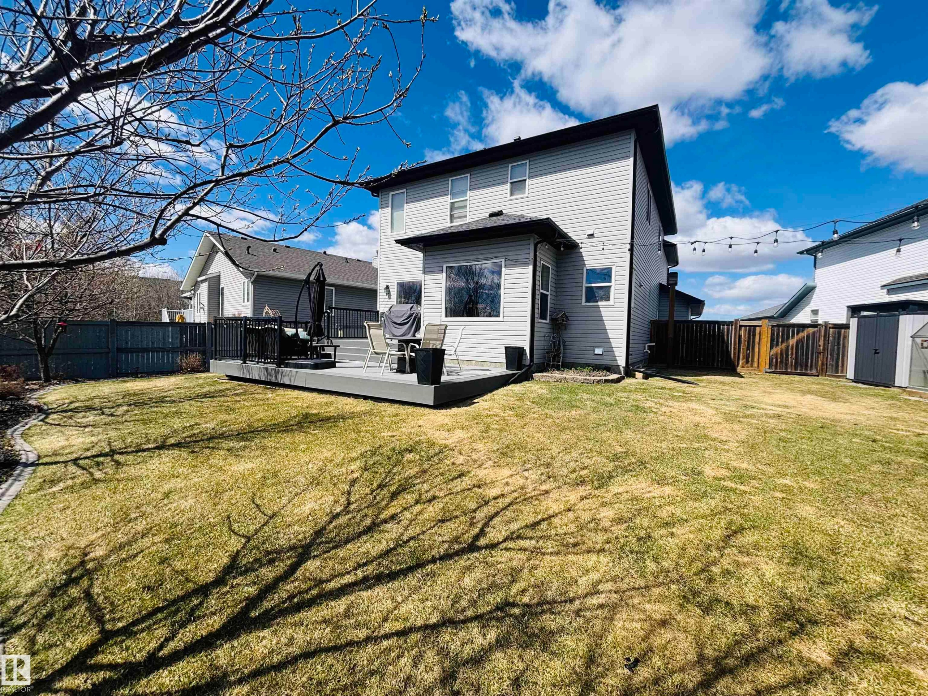 Expansive backyard featuring a multi-level composite deck with dark railings, a manicured lawn, and a privacy fence - 112 Lakeland Point(E), Beaumont, AB - Outdoor