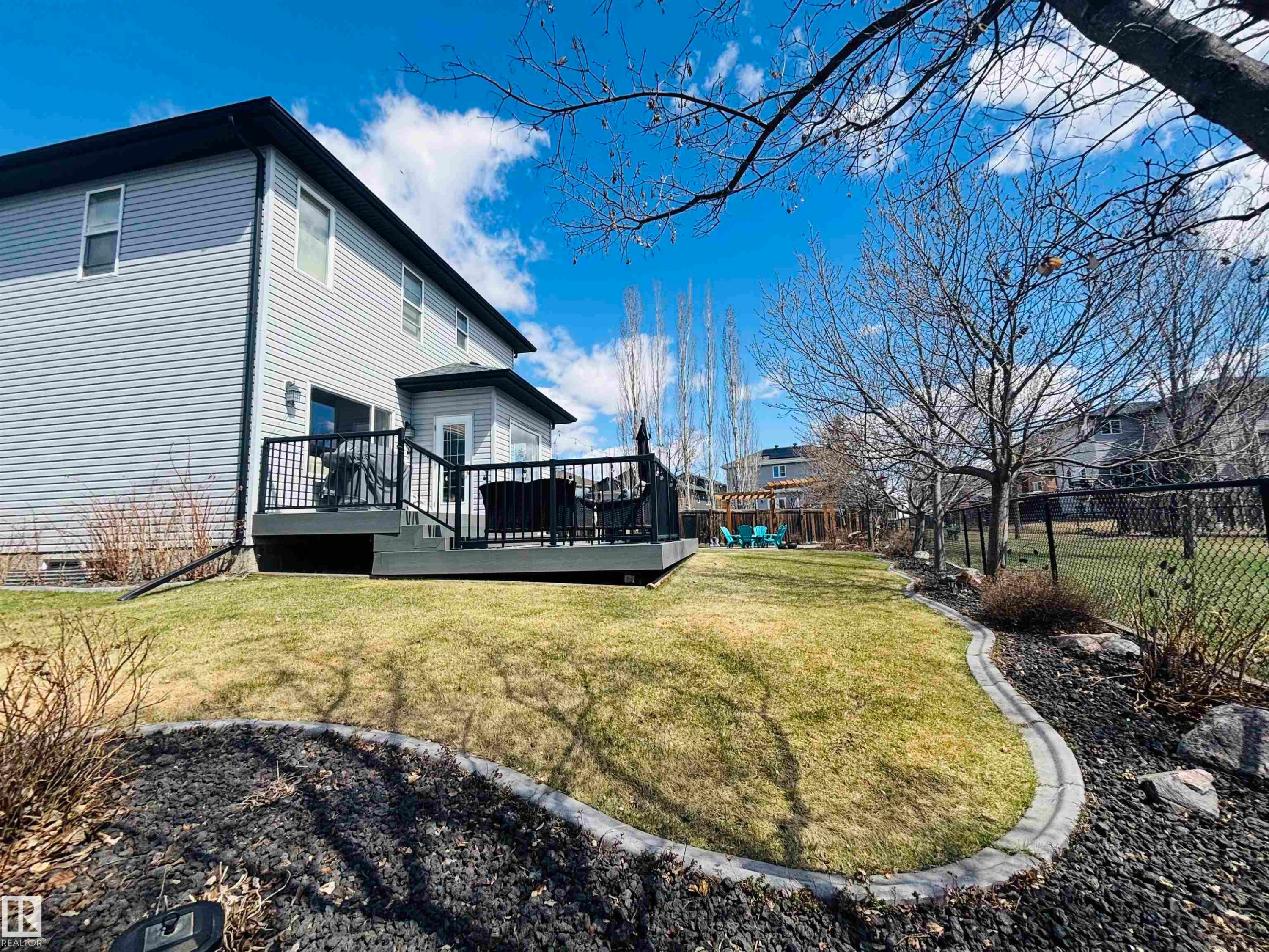 Spacious backyard featuring a large deck with black railings, a manicured lawn, and mature trees - 112 Lakeland Point(E), Beaumont, AB - Outdoor With Deck Patio Veranda