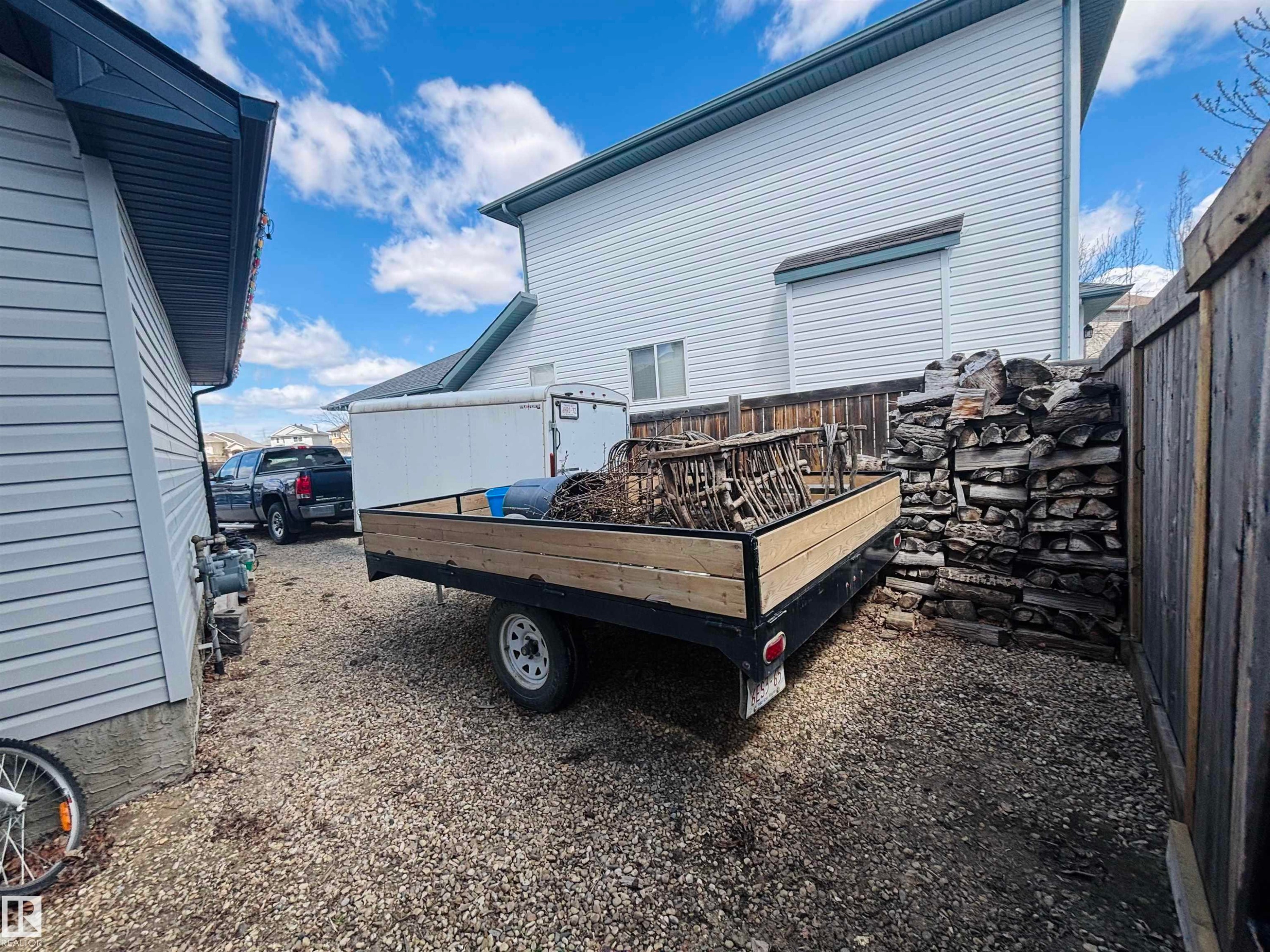 Gravel side yard featuring a wooden privacy fence and a stacked woodpile - 112 Lakeland Point(E), Beaumont, AB - Outdoor With Exterior