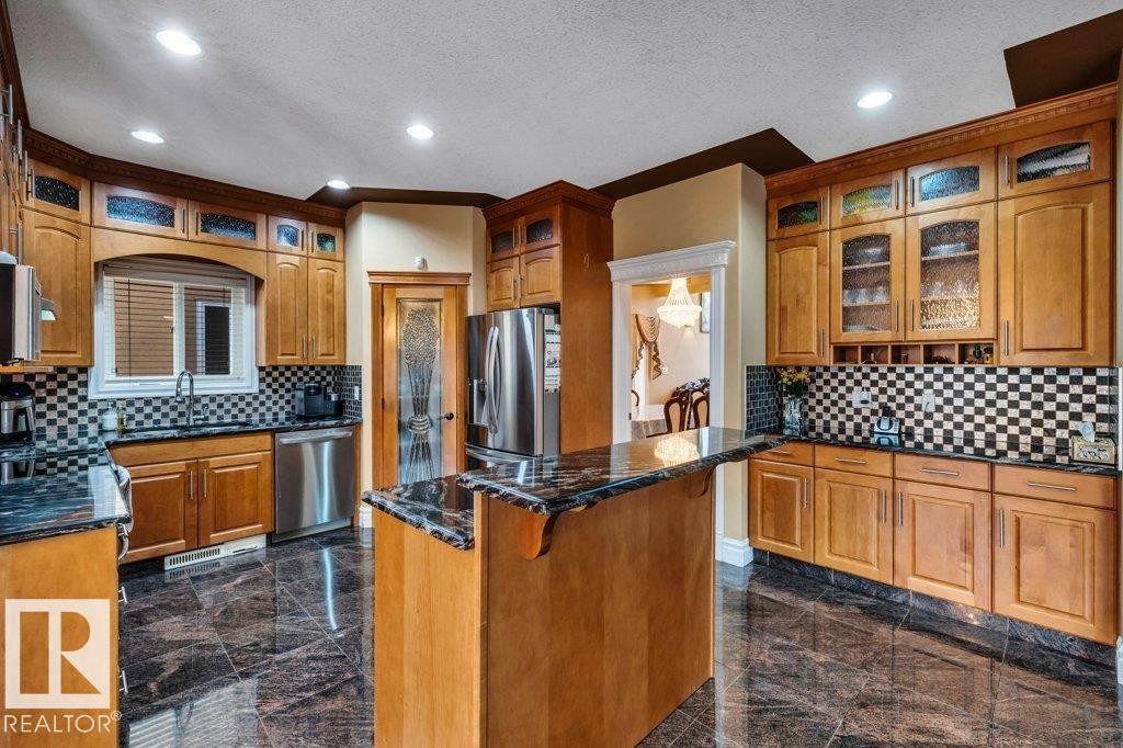 Kitchen featuring extensive wood cabinetry, dark stone countertops, stainless steel appliances, a checkerboard tile backsplash, and dark tile flooring - 816 Wildwood Crescent, Edmonton, AB - Indoor Photo Showing Kitchen