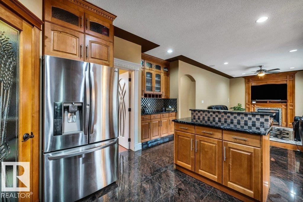 Kitchenette featuring a stainless steel French door refrigerator, wood-finish cabinetry, dark granite countertops, and a black and white tiled backsplash - 816 Wildwood Crescent, Edmonton, AB - Indoor Photo Showing Kitchen