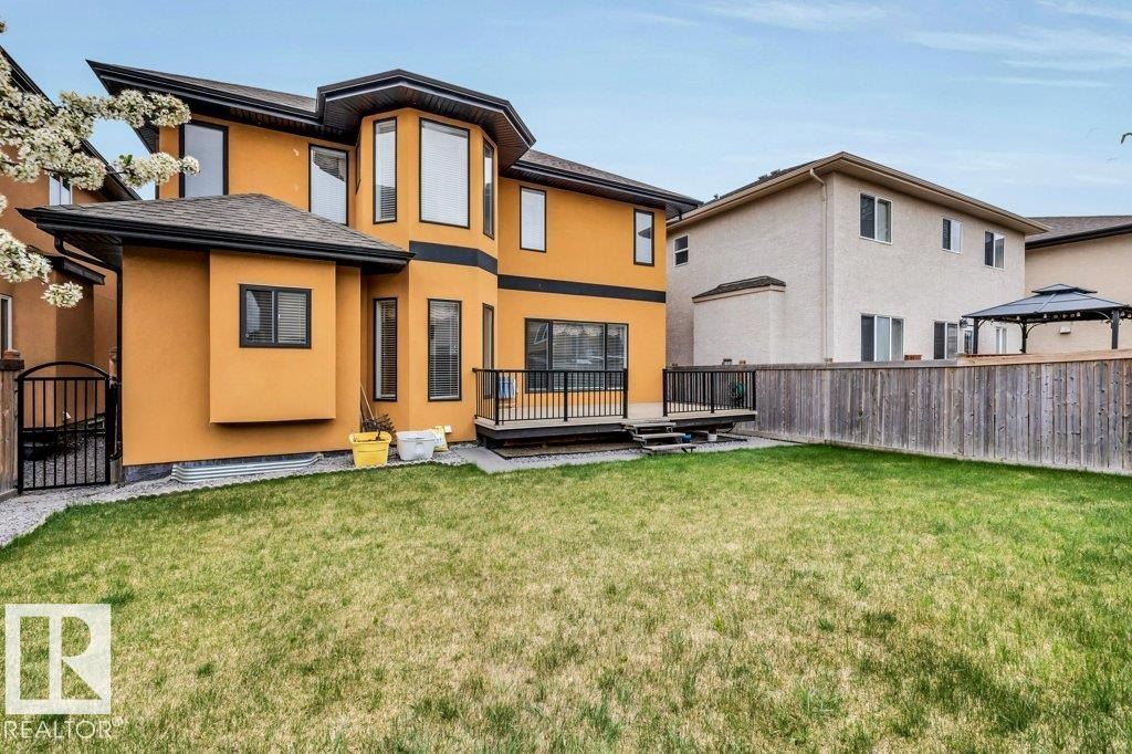 Expansive green space featuring a contemporary stucco exterior, a black wrought iron gate, a raised deck with dark railings, and a wood privacy fence - 816 Wildwood Crescent, Edmonton, AB - Outdoor