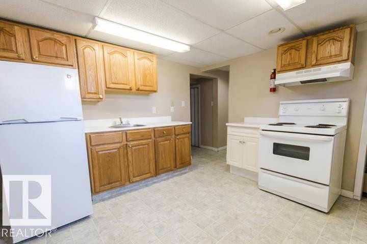 The kitchen features a white refrigerator, a white stove with an overhead range hood, and light wood cabinetry with white countertops - 10806 64 Avenue, Edmonton, AB - Indoor Photo Showing Kitchen