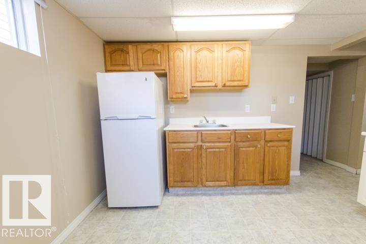 The property features a kitchen area with wood cabinetry, a white countertop, and a white refrigerator - 10806 64 Avenue, Edmonton, AB - Indoor Photo Showing Kitchen