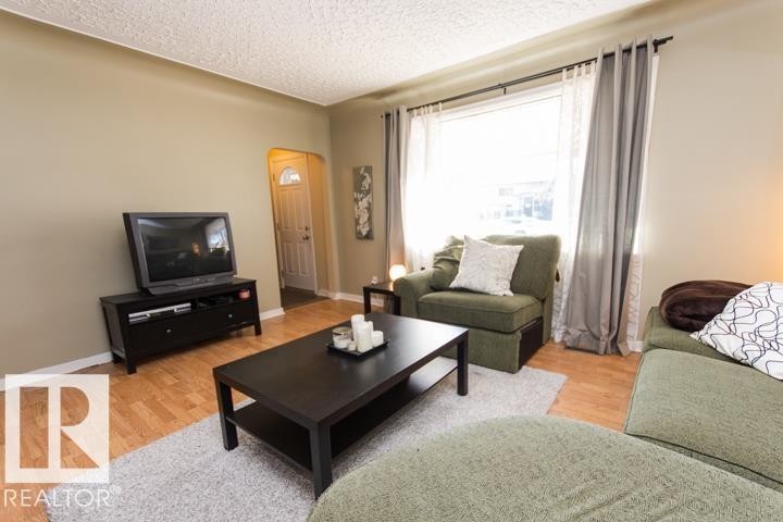 Living room featuring light-colored walls, light wood flooring, and a large window with sheer and opaque curtains - 10806 64 Avenue, Edmonton, AB - Indoor Photo Showing Living Room