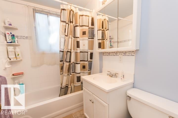 The bathroom features a white bathtub, a window, a white vanity with a sink, and a toilet - 10806 64 Avenue, Edmonton, AB - Indoor Photo Showing Bathroom