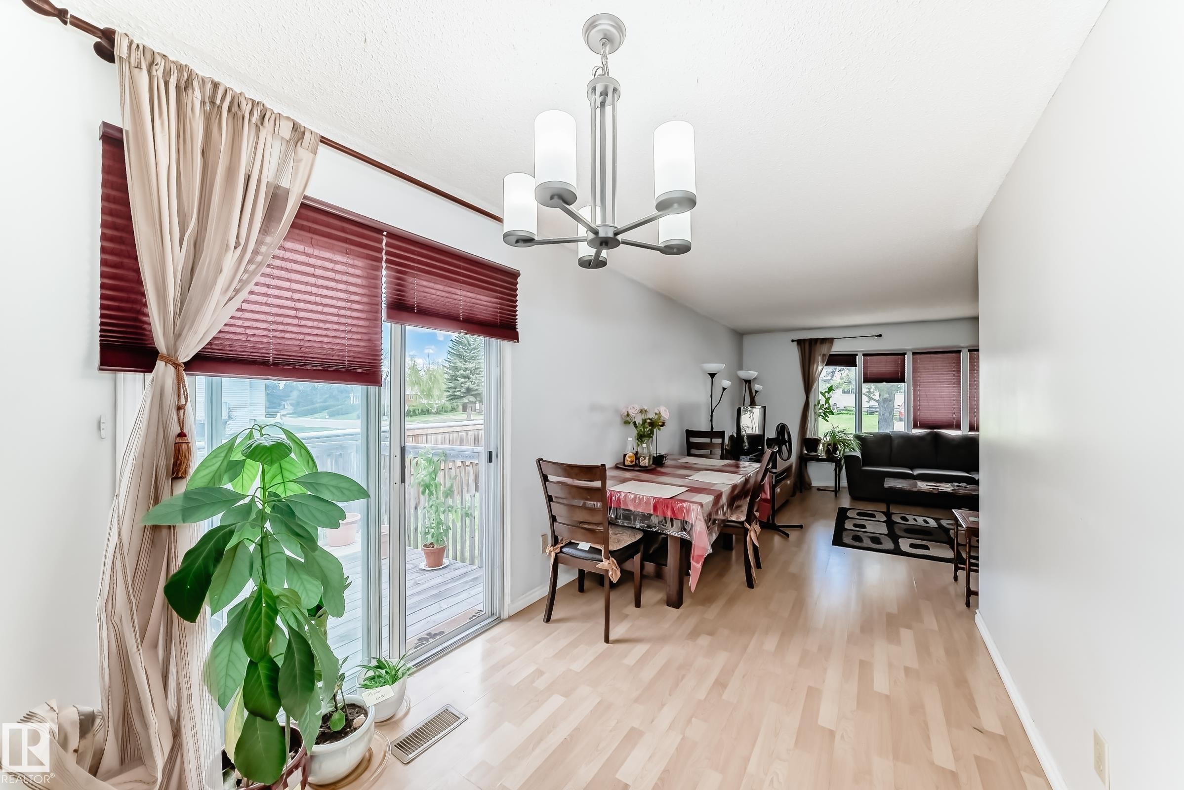 Open-concept dining area with wood-finish flooring, a modern chandelier, and access to an outdoor deck through sliding glass doors - 1804 51 Street Nw, Edmonton, AB - Indoor