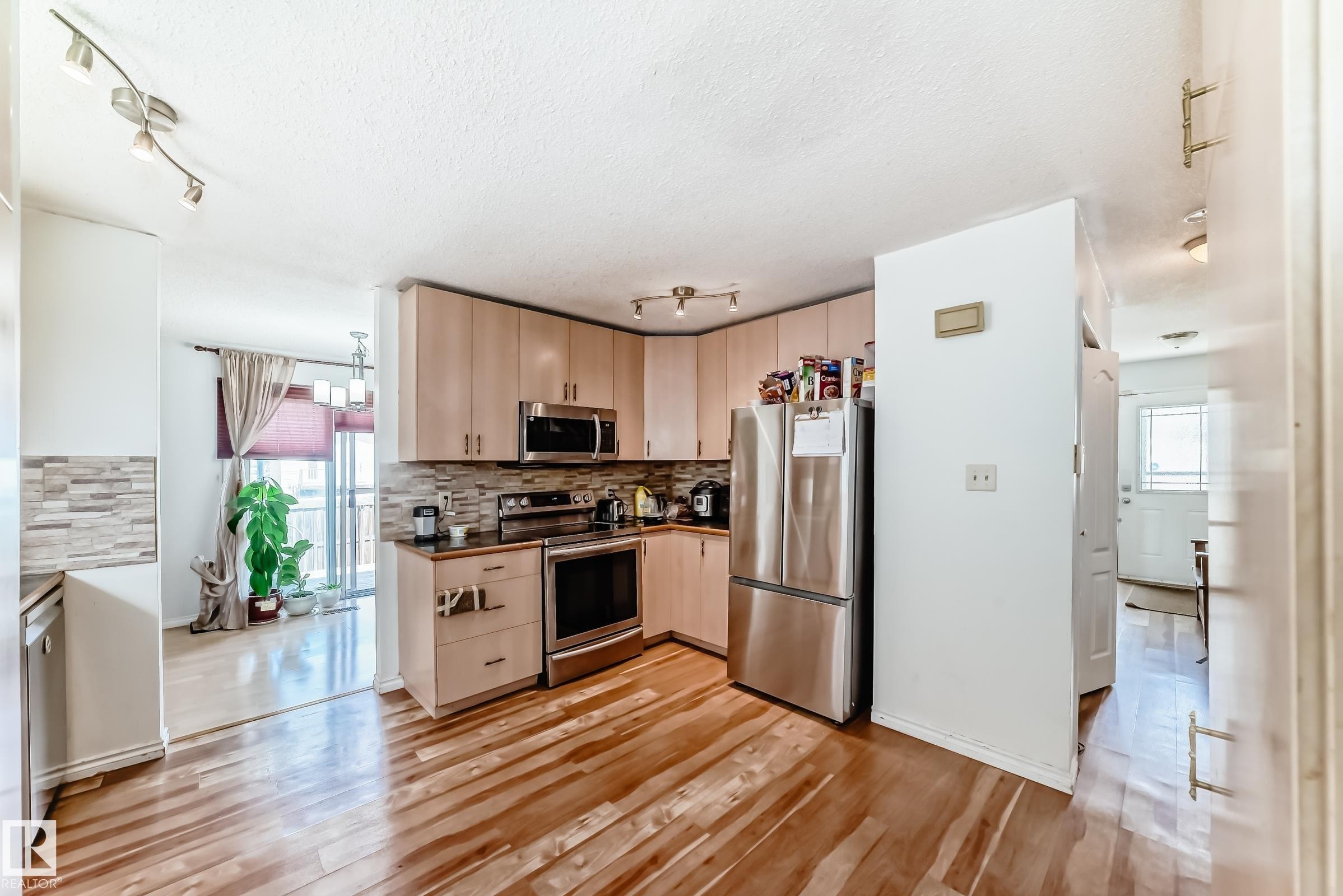 Modern kitchen featuring stainless steel appliances, light wood-finish cabinetry, a stone tile backsplash, dark countertops, and wood-finish flooring - 1804 51 Street Nw, Edmonton, AB - Indoor Photo Showing Kitchen