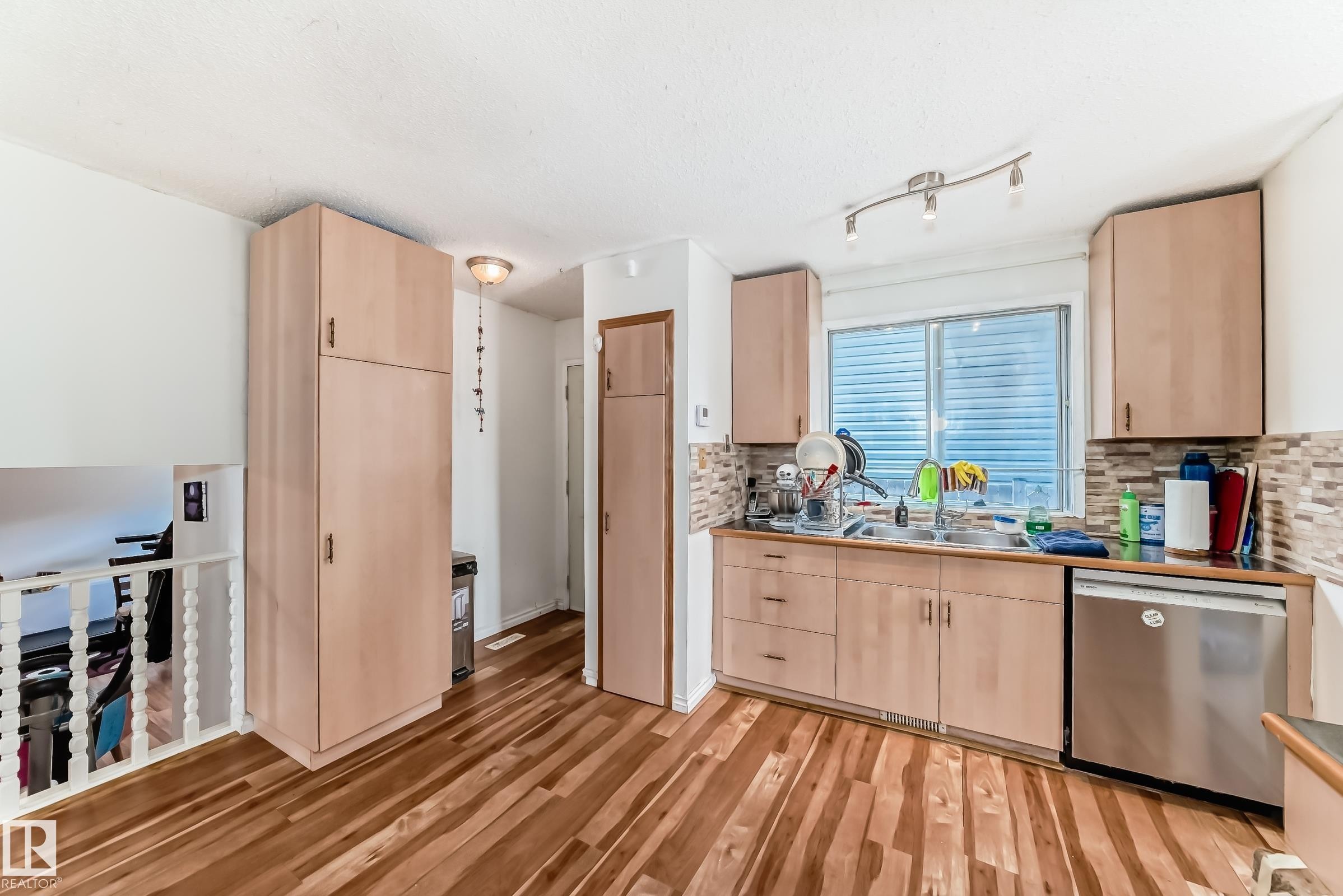 Kitchen area featuring wood-finish flooring, light wood cabinetry, and a patterned tile backsplash - 1804 51 Street Nw, Edmonton, AB - Indoor Photo Showing Kitchen With Double Sink