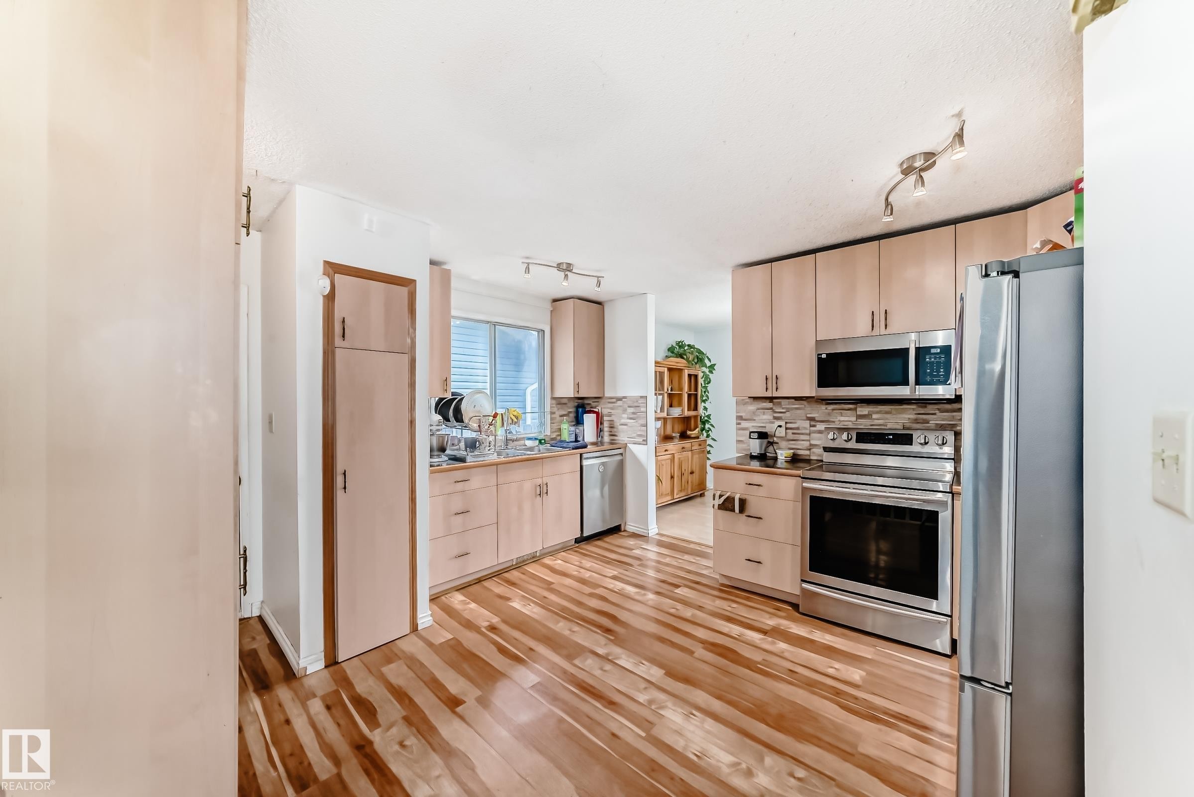 Kitchen featuring wood-finish flooring, light-toned cabinetry, a mosaic tile backsplash, and stainless steel appliances including an oven range, microwave, and refrigerator - 1804 51 Street Nw, Edmonton, AB - Indoor Photo Showing Kitchen
