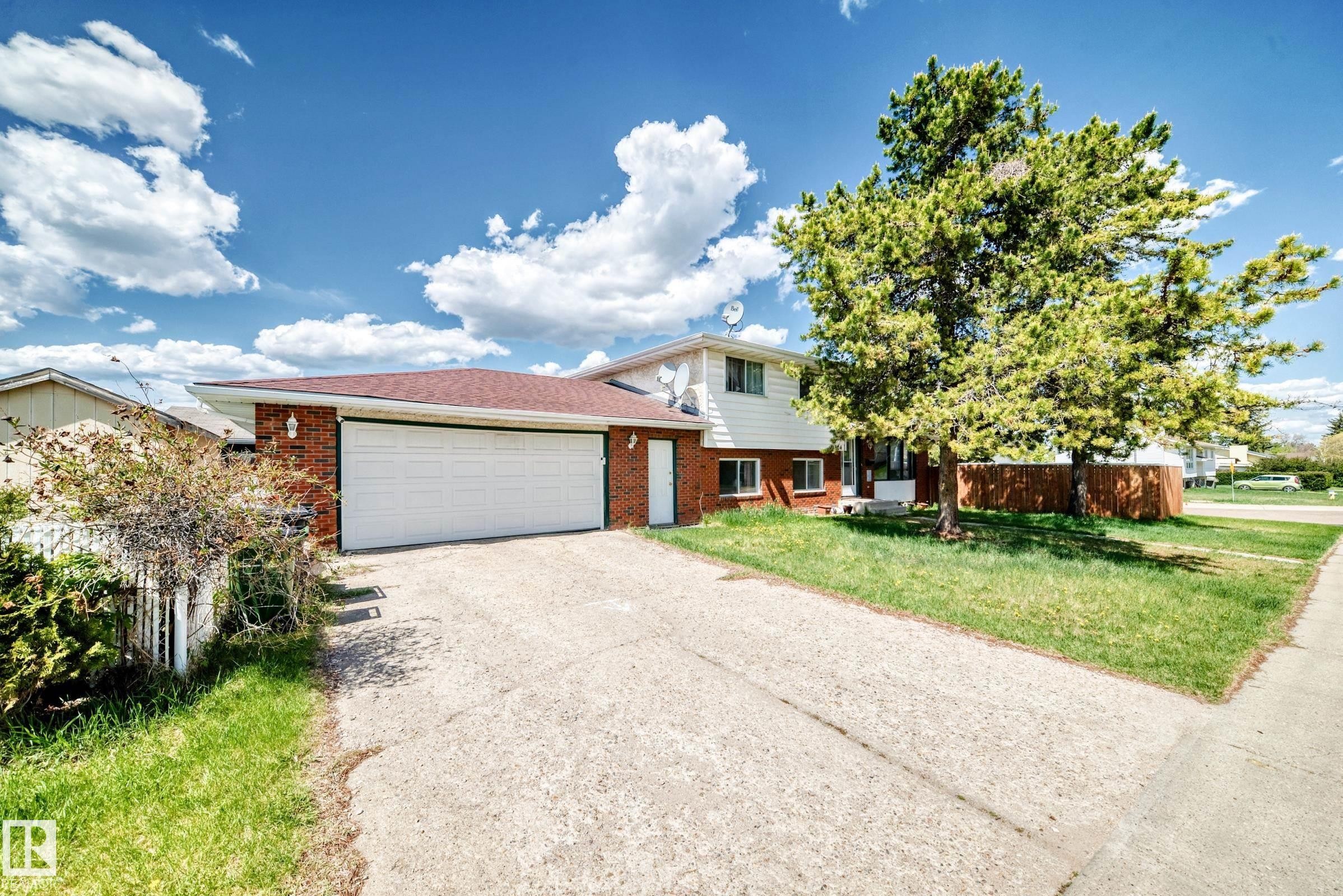 Brick and siding exterior featuring an attached garage, paved driveway, mature trees, and a red shingle roof - 1804 51 Street Nw, Edmonton, AB - Outdoor