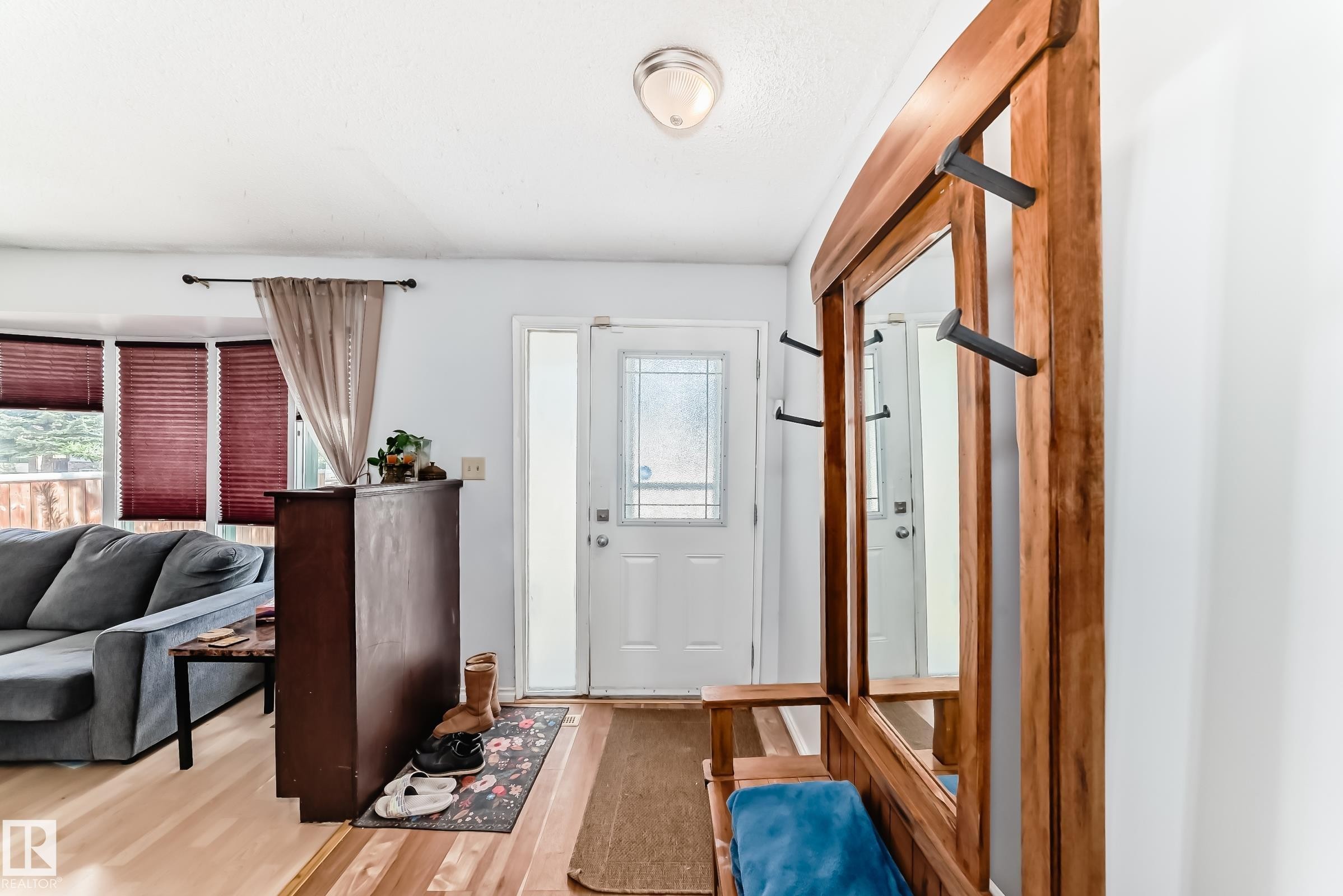 Entryway featuring a white door with decorative glass, light wood-finish flooring, and a built-in wood-frame mirror with integrated coat hooks - 1804 51 Street Nw, Edmonton, AB - Indoor Photo Showing Other Room