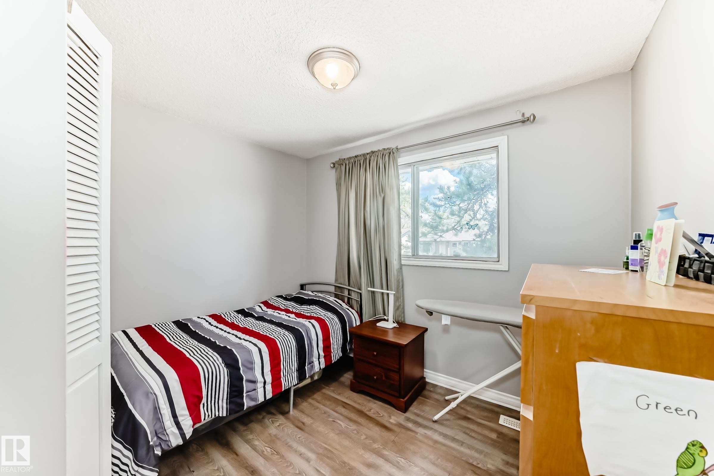 Room featuring wood-finish flooring, a window with exterior views, and a louvered bi-fold closet door - 1804 51 Street Nw, Edmonton, AB - Indoor Photo Showing Bedroom
