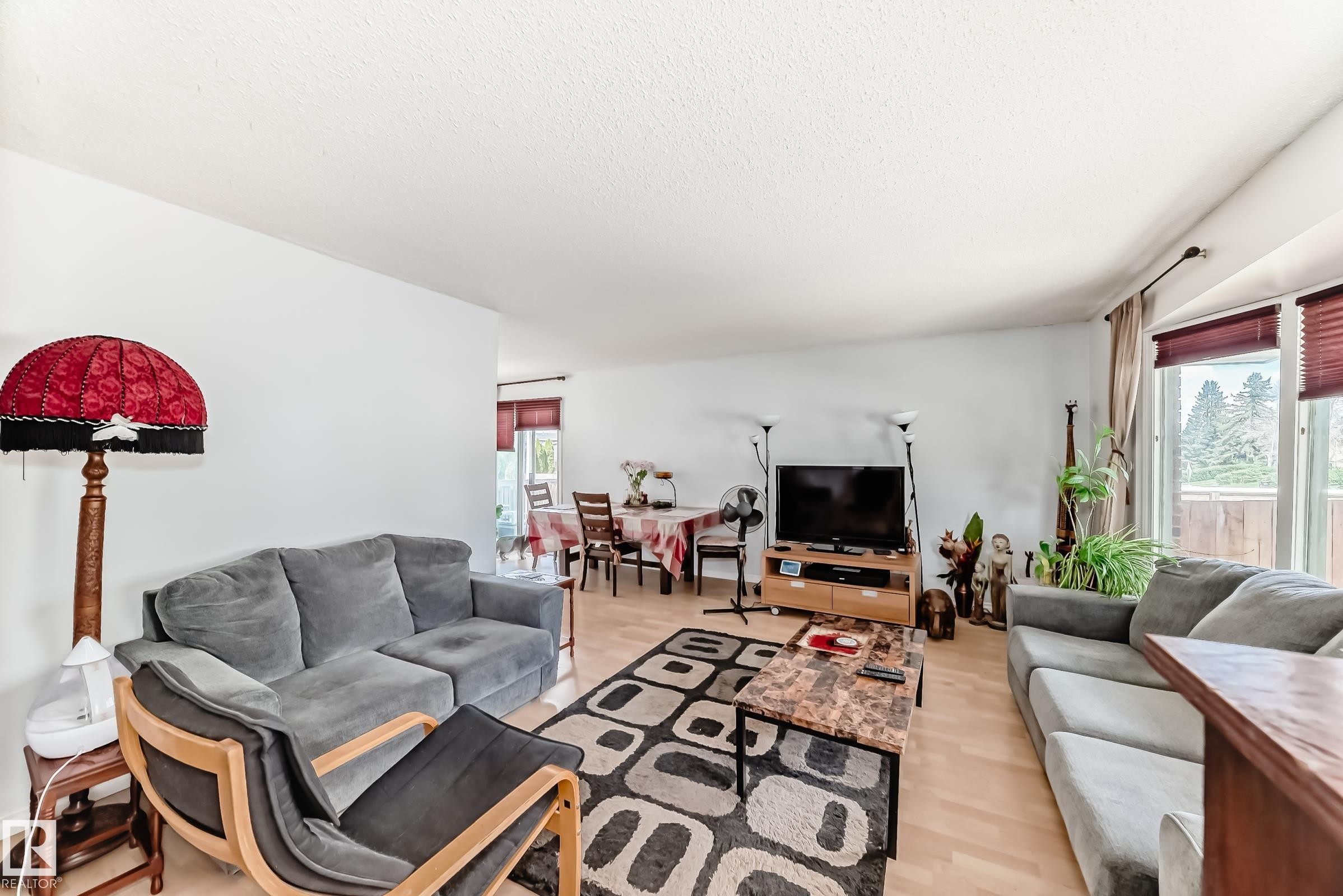 Open-concept living space featuring light wood-finish flooring, white walls, and prominent windows with horizontal blinds - 1804 51 Street Nw, Edmonton, AB - Indoor Photo Showing Living Room