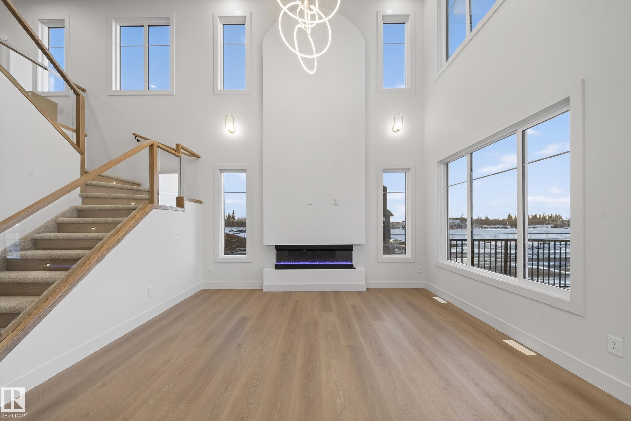 Two-story living room featuring expansive windows, a modern fireplace, wood-finish flooring, and a contemporary chandelier - 4276 Charles Close, Edmonton, AB - Indoor Photo Showing Other Room