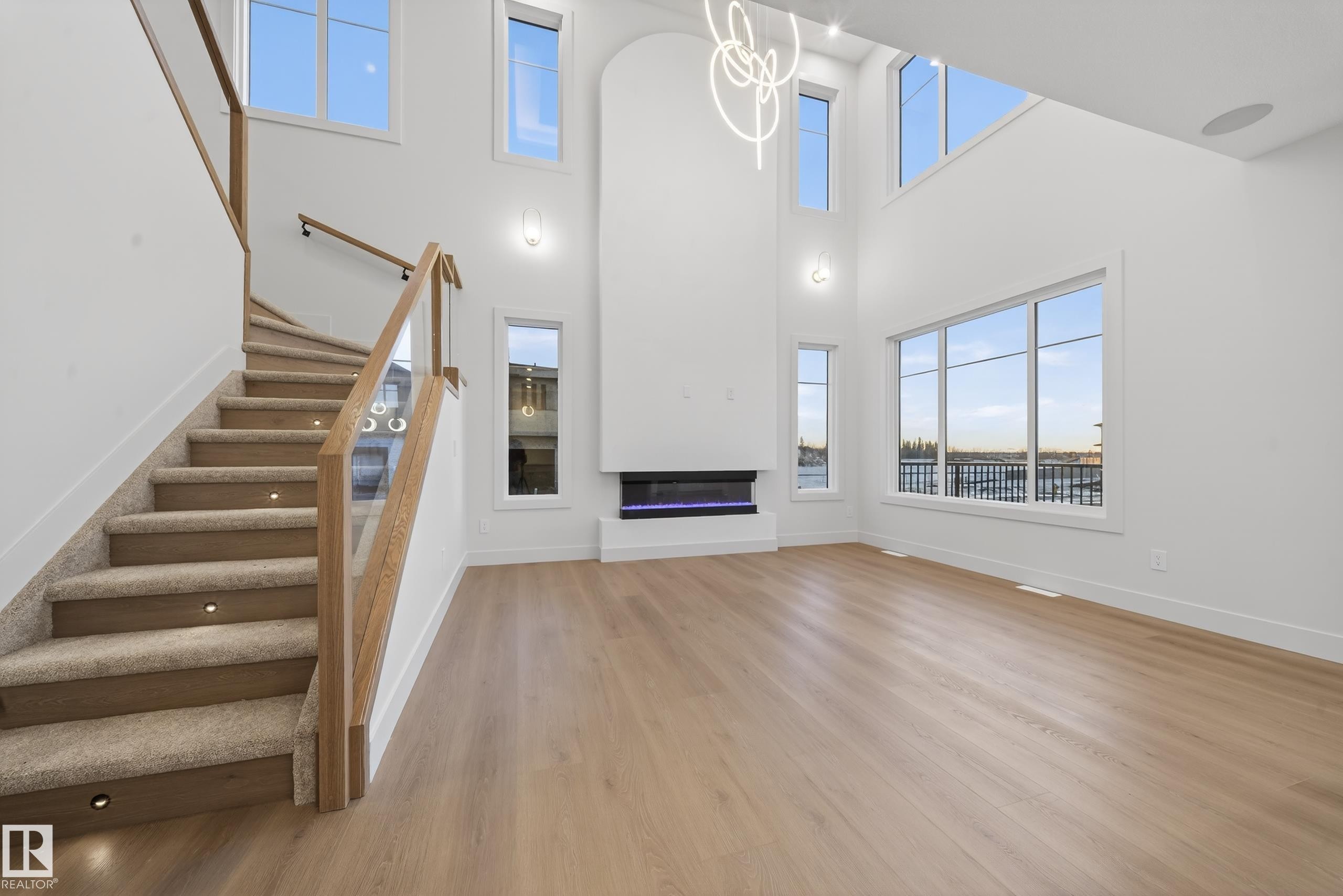 Spacious living area featuring light wood-finish flooring, a two-story fireplace with an integrated electric insert, and large windows providing abundant natural light - 4276 Charles Close, Edmonton, AB - Indoor Photo Showing Other Room