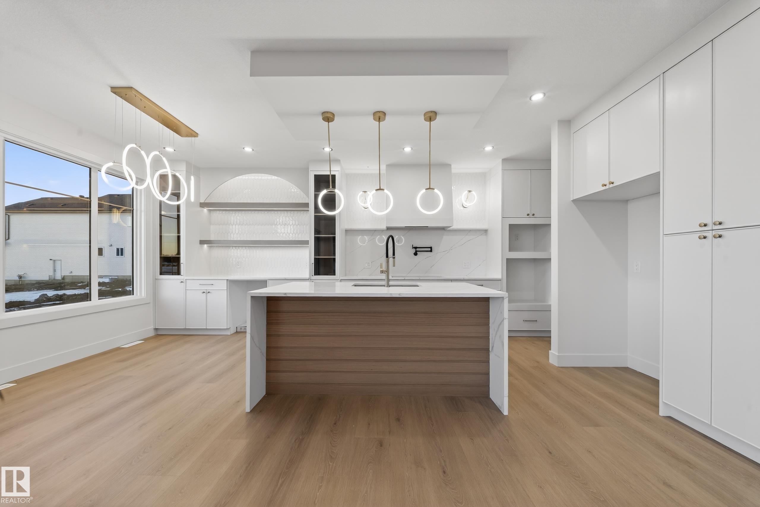 Modern kitchen featuring a waterfall-edge island with wood-finish paneling, white shaker cabinetry, and light wood-finish flooring - 4276 Charles Close, Edmonton, AB - Indoor Photo Showing Kitchen