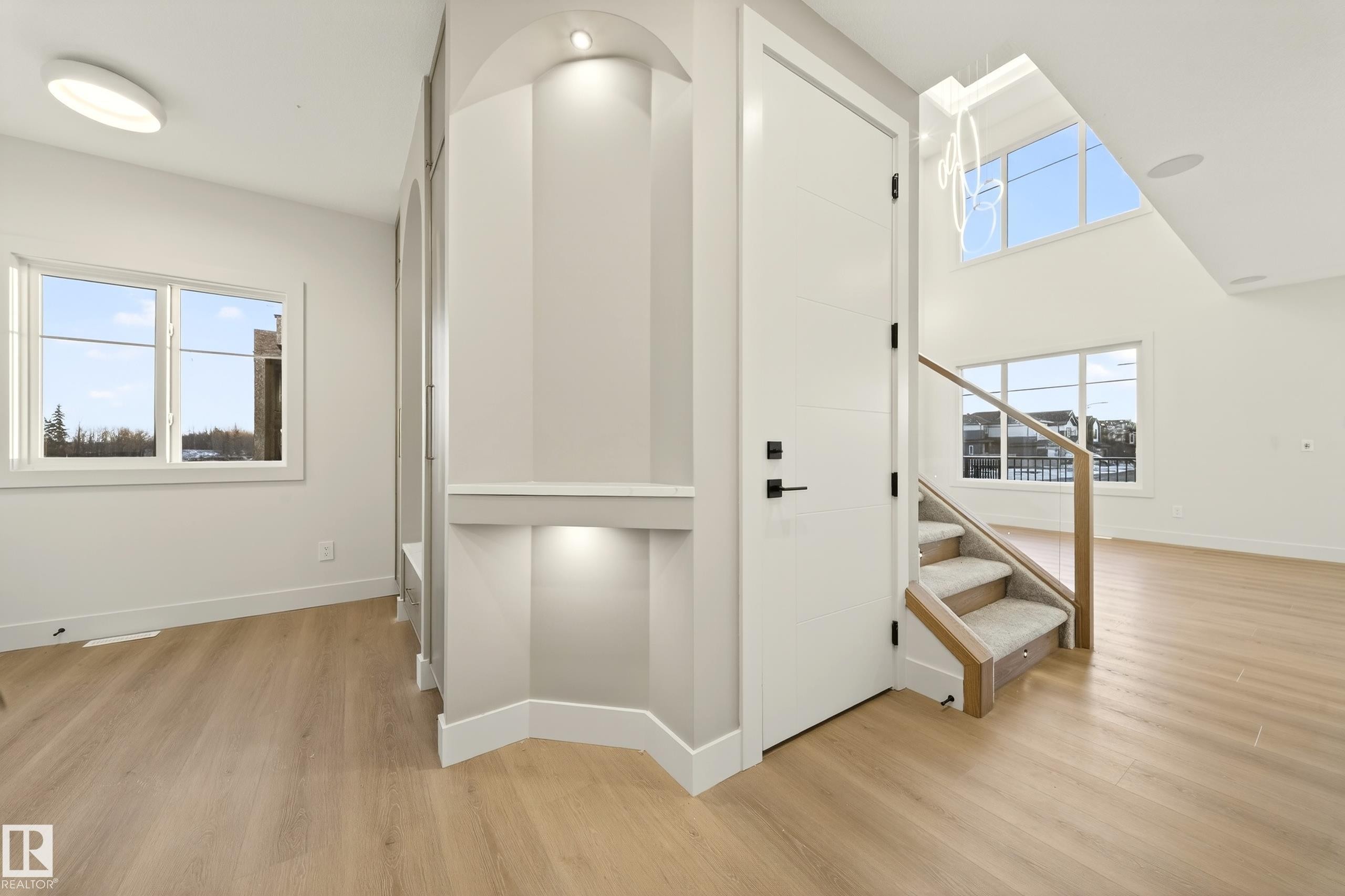 Open-concept interior featuring light wood-finish flooring, a two-story ceiling with high windows, and a staircase with glass railings - 4276 Charles Close, Edmonton, AB - Indoor Photo Showing Other Room