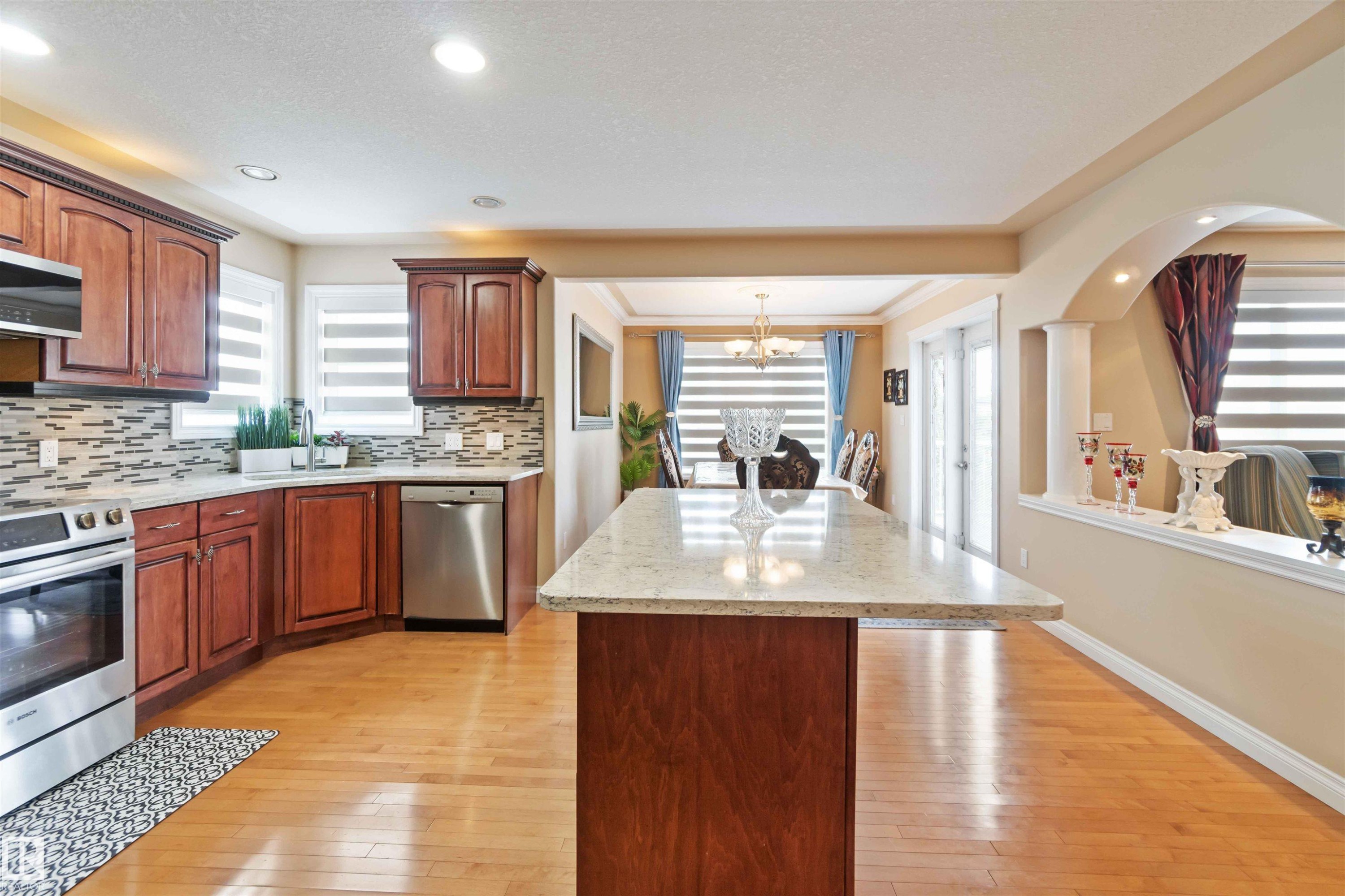 Kitchen featuring wood-finish flooring, dark wood cabinetry, stainless steel appliances, and a mosaic tile backsplash - 6116 53 Avenue, Beaumont, AB - Indoor Photo Showing Kitchen With Stainless Steel Kitchen With Double Sink With Upgraded Kitchen