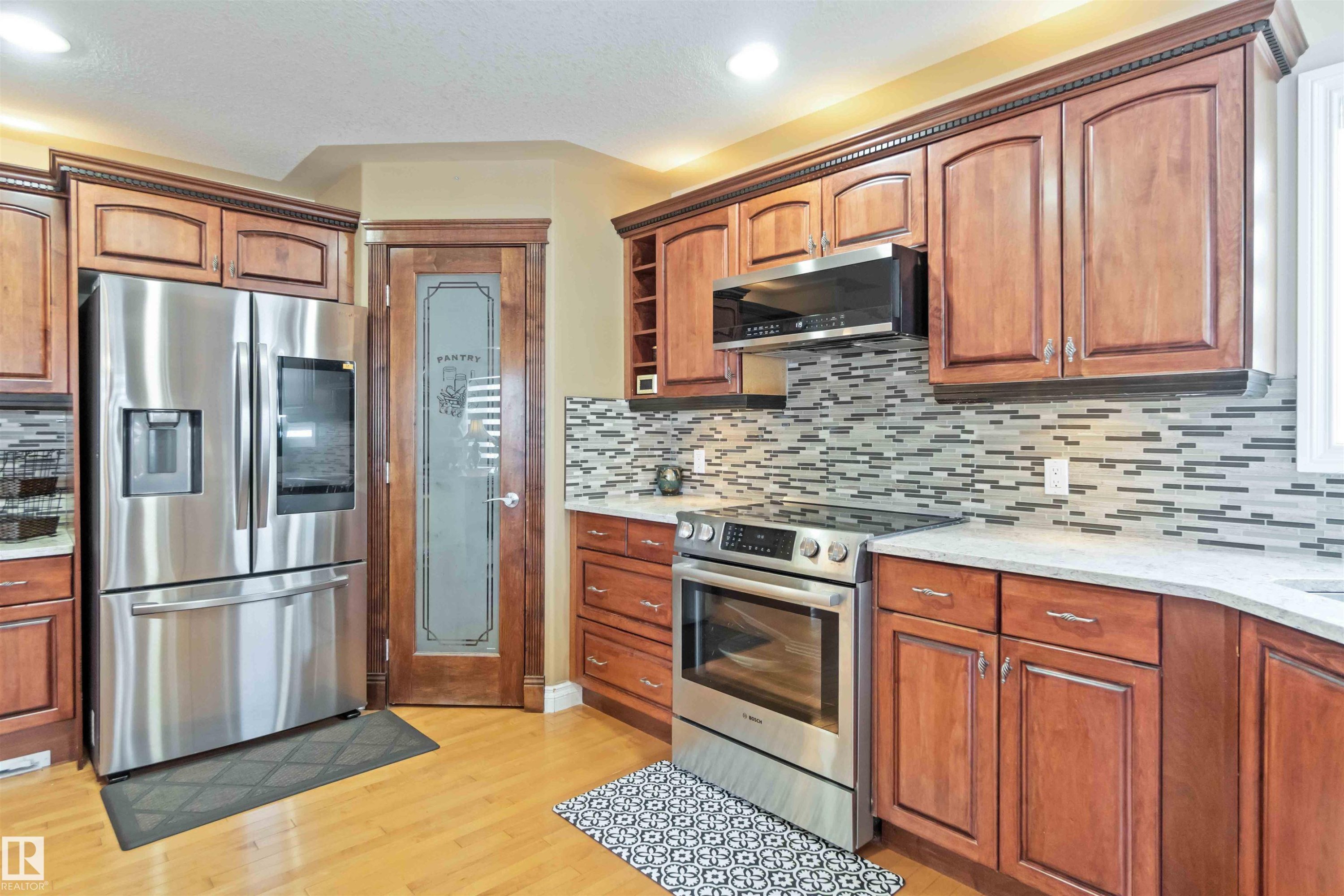 Kitchen featuring wood-finish cabinetry, stainless steel appliances, a mosaic tile backsplash, and light-toned countertops - 6116 53 Avenue, Beaumont, AB - Indoor Photo Showing Kitchen With Stainless Steel Kitchen With Upgraded Kitchen