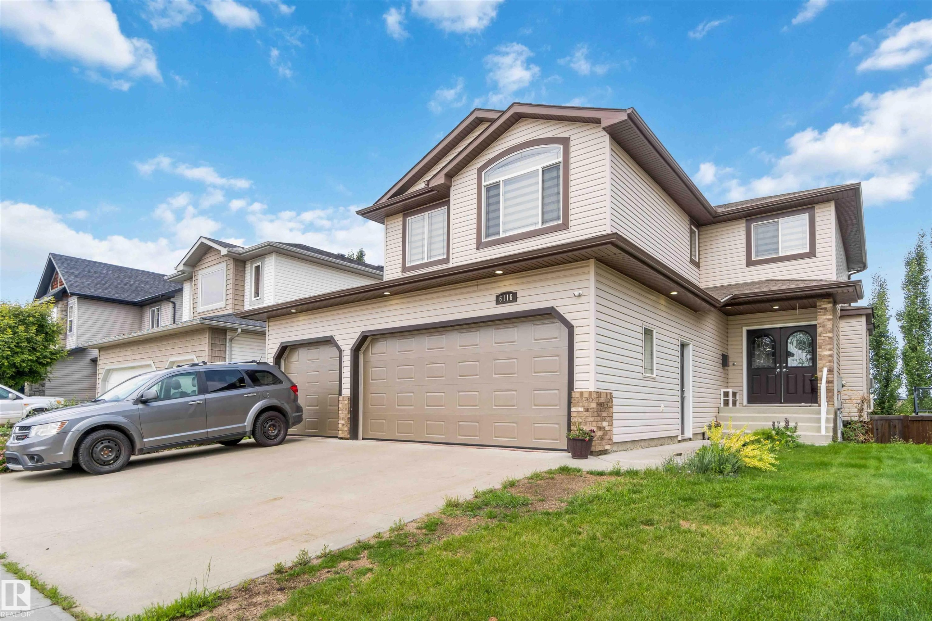 Two-story residence featuring light-toned horizontal siding, a double front entry door with decorative glass, and a two-car garage with individual doors - 6116 53 Avenue, Beaumont, AB - Outdoor