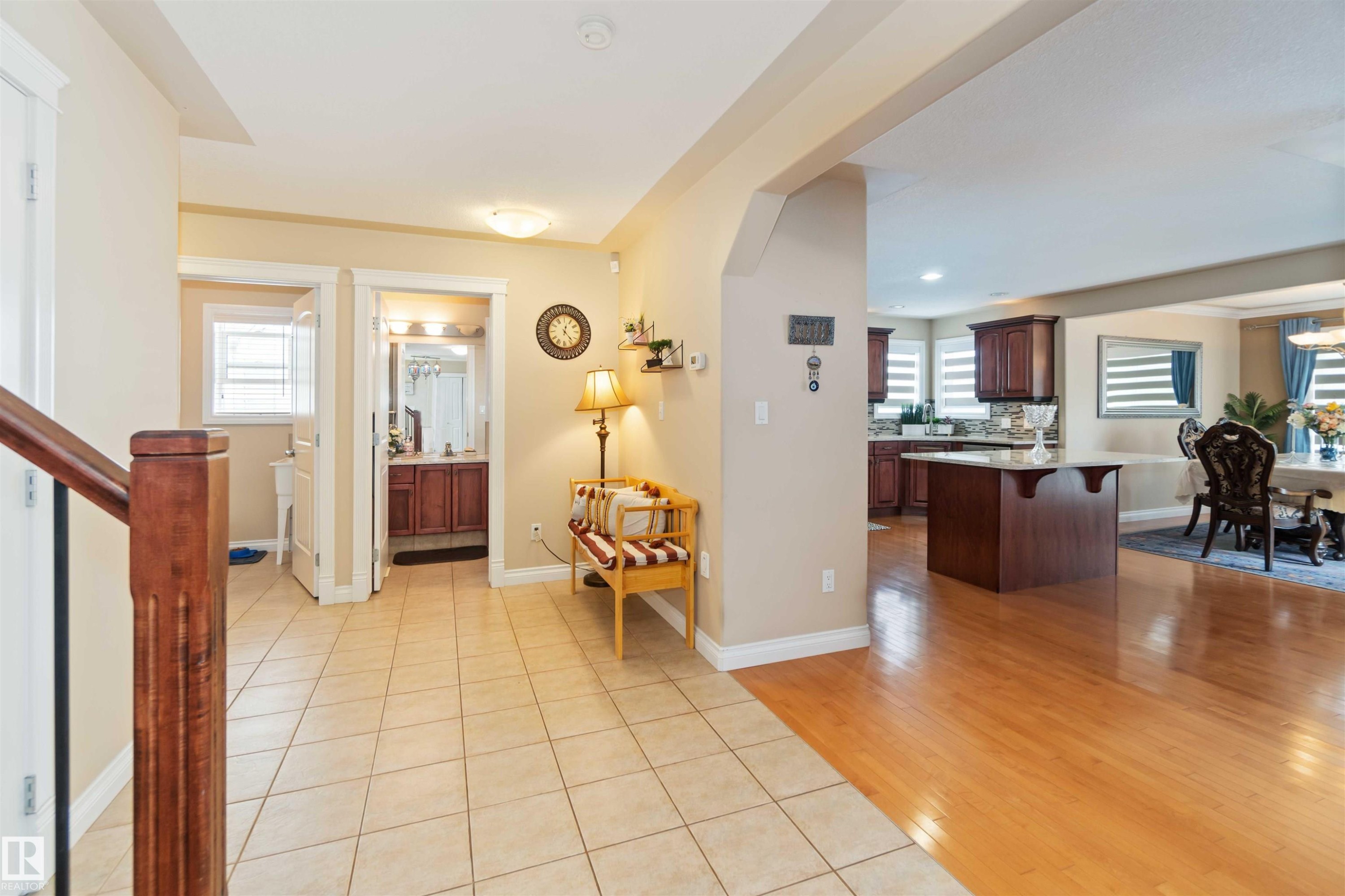 Entryway featuring light-toned tile flooring, a wood staircase, and a doorway leading to a powder room with a pedestal sink - 6116 53 Avenue, Beaumont, AB - Indoor Photo Showing Other Room