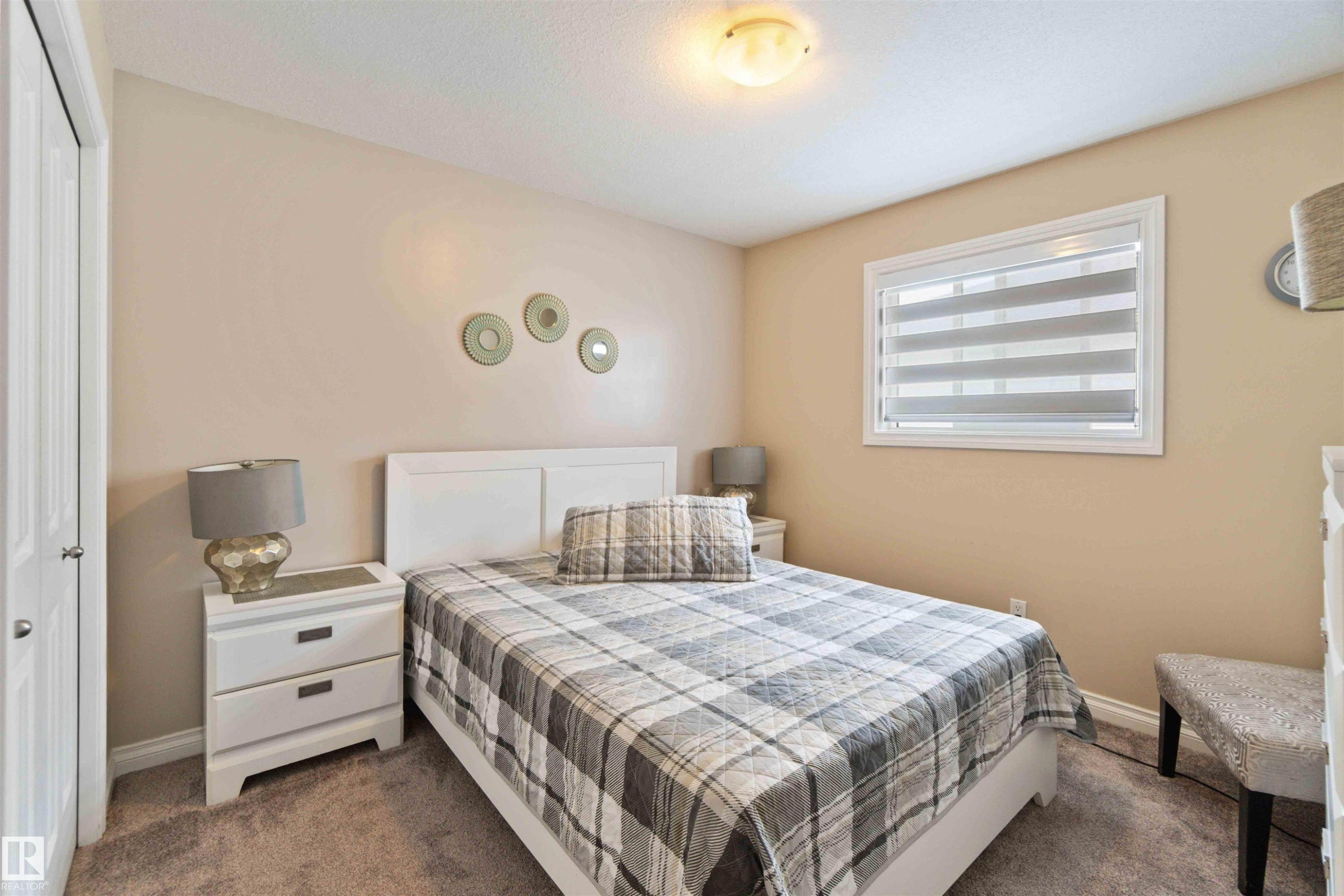 Carpeted room with a window featuring horizontal blinds and a ceiling-mounted light fixture - 6116 53 Avenue, Beaumont, AB - Indoor Photo Showing Bedroom