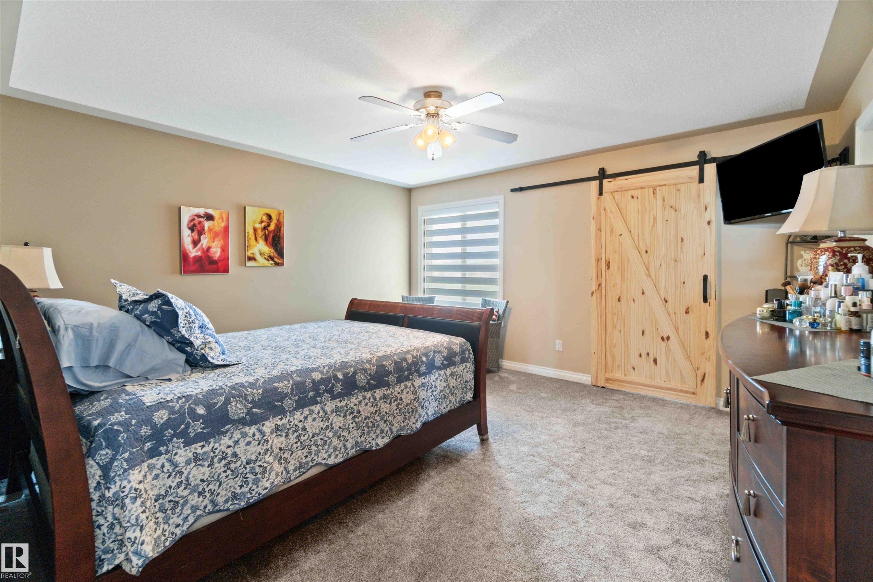 Tray ceiling with recessed lighting and a ceiling fan, light wood-finish barn door with black hardware, neutral tone walls, and soft carpet flooring - 6116 53 Avenue, Beaumont, AB - Indoor Photo Showing Bedroom