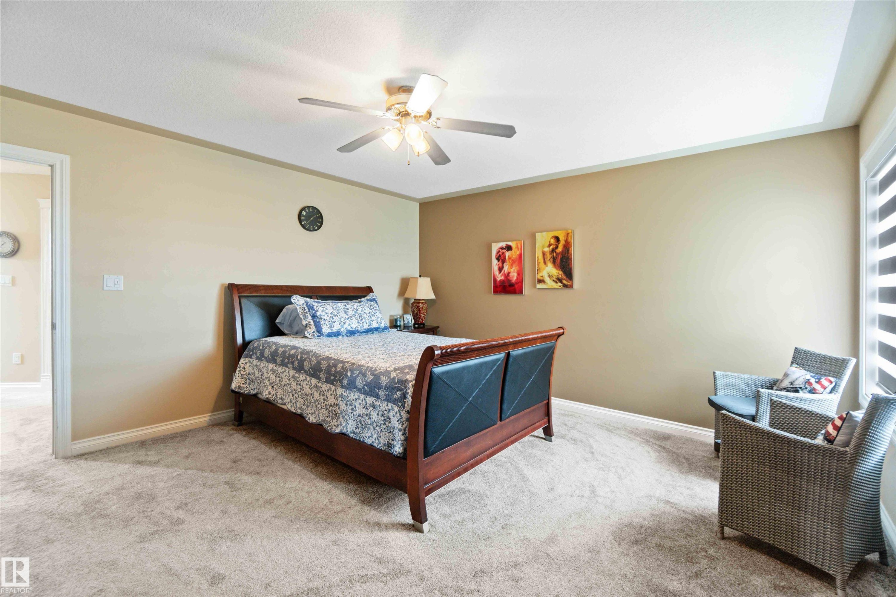 Carpeted room featuring a ceiling fan with integrated lighting, a tray ceiling, and a window with horizontal blinds - 6116 53 Avenue, Beaumont, AB - Indoor Photo Showing Bedroom