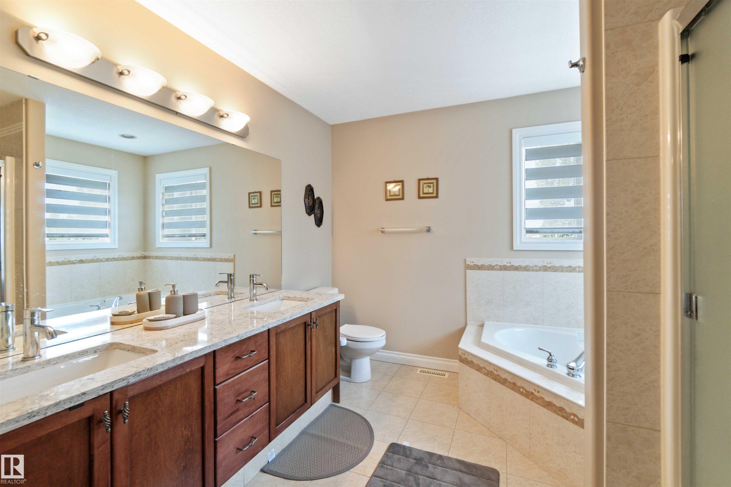 Bathroom featuring a double vanity with granite-style countertop, dual undermount sinks, and wood cabinetry - 6116 53 Avenue, Beaumont, AB - Indoor Photo Showing Bathroom